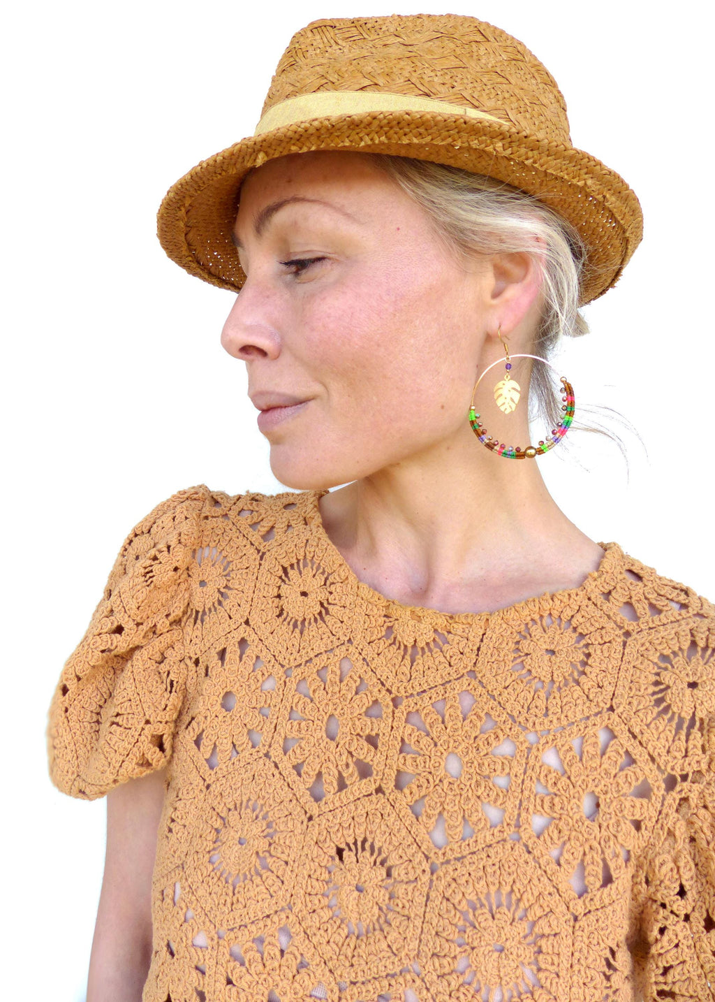 Peut inclure: Une femme portant un chapeau de paille et un haut en crochet avec des boucles d'oreilles créoles en perles colorées ornées d'un pendentif en feuille d'or.