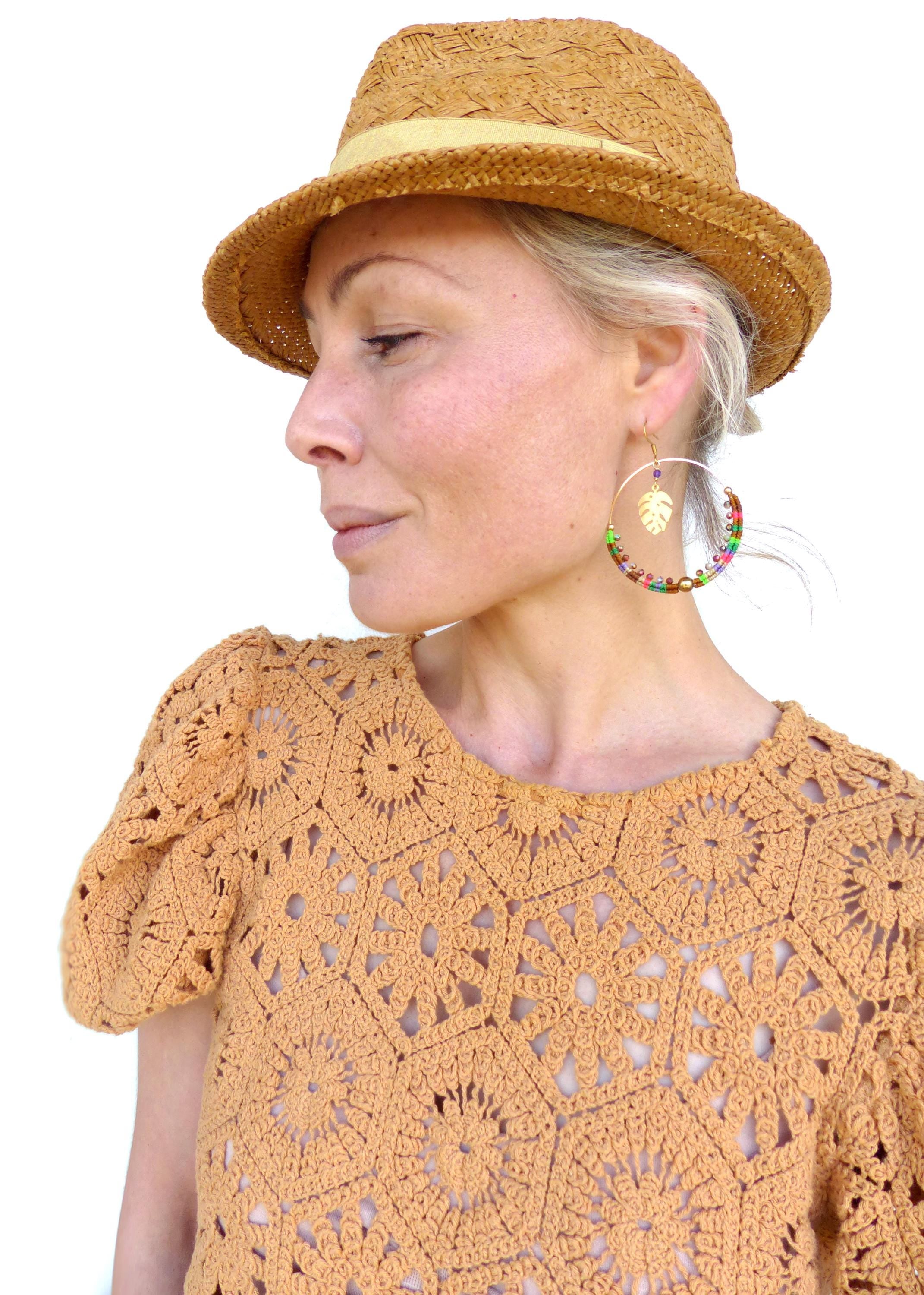 Peut inclure: Une femme portant un chapeau de paille et un haut en crochet avec des boucles d'oreilles créoles en perles colorées ornées d'un pendentif en feuille d'or.