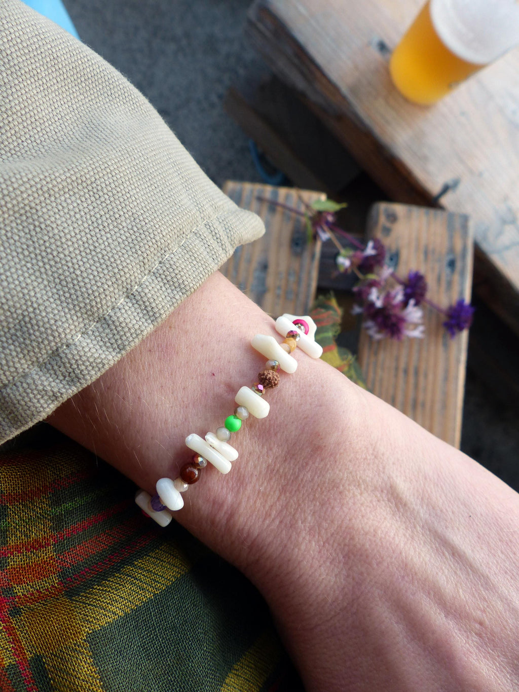 Peut inclure: Un bracelet composé de perles blanches, brunes, vertes et roses. Le bracelet est porté au poignet.