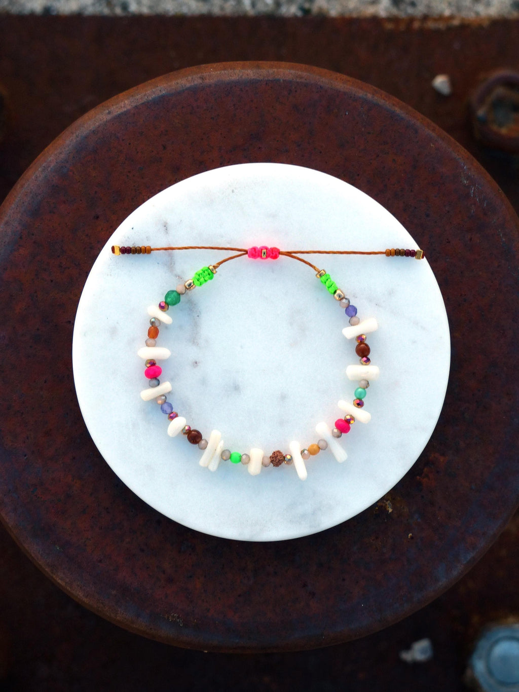 Peut inclure: Un bracelet coloré en perles avec des perles blanches, roses, vertes, brunes et violettes. Le bracelet est attaché avec un cordon brun et a un accent rose et vert.