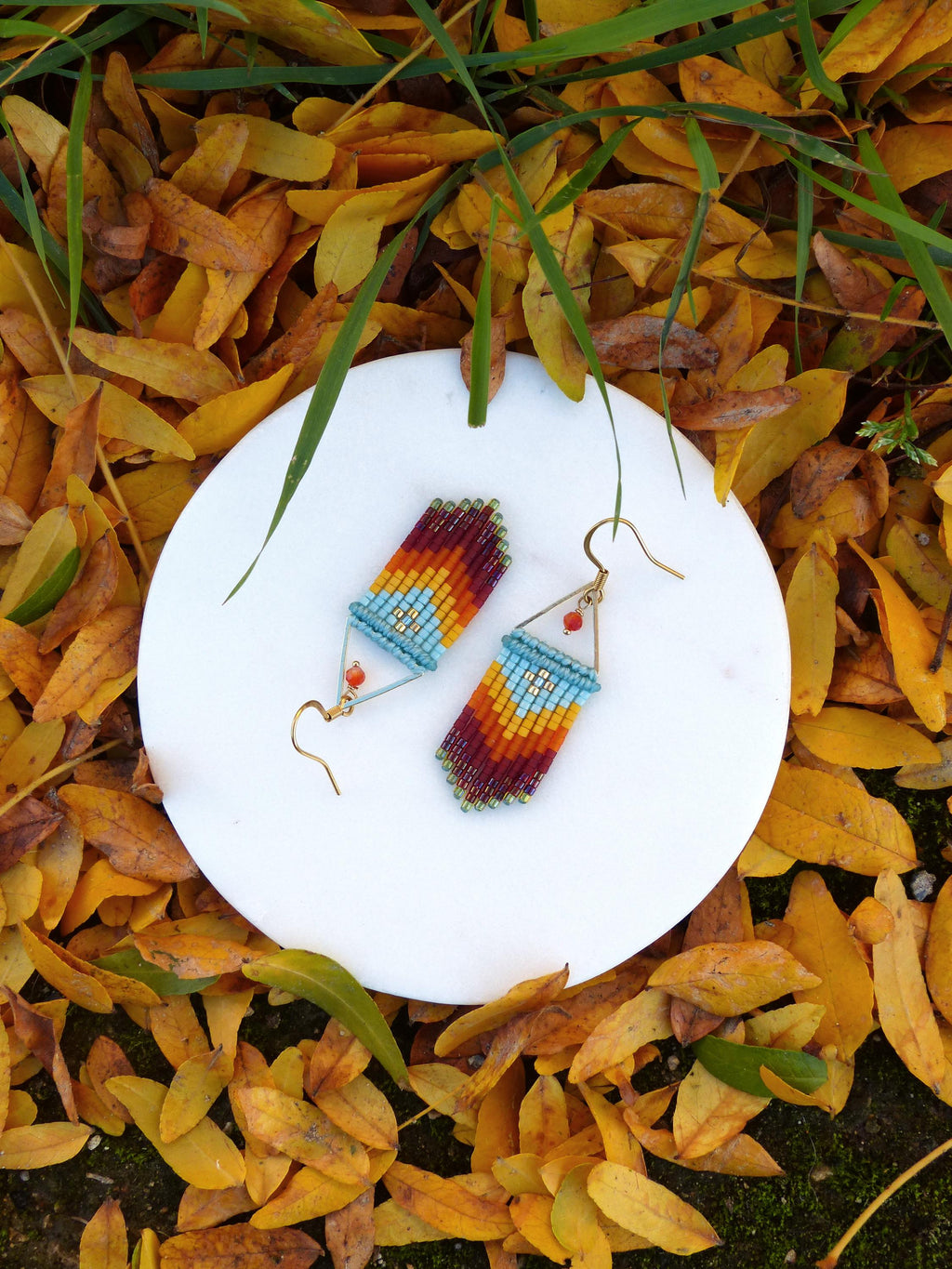 Peut inclure: Une paire de boucles d'oreilles en perles colorées avec un motif géométrique. Les boucles d'oreilles sont faites de petites perles colorées dans des tons de rouge, orange, jaune, bleu et vert. Les boucles d'oreilles sont suspendues à des crochets dorés.