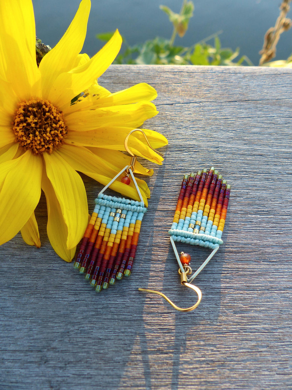 Peut inclure: Une paire de boucles d'oreilles en perles avec un motif géométrique. Les boucles d'oreilles sont faites de petites perles colorées dans des tons de rouge, orange, jaune, bleu et vert. Les boucles d'oreilles sont suspendues à des crochets dorés.
