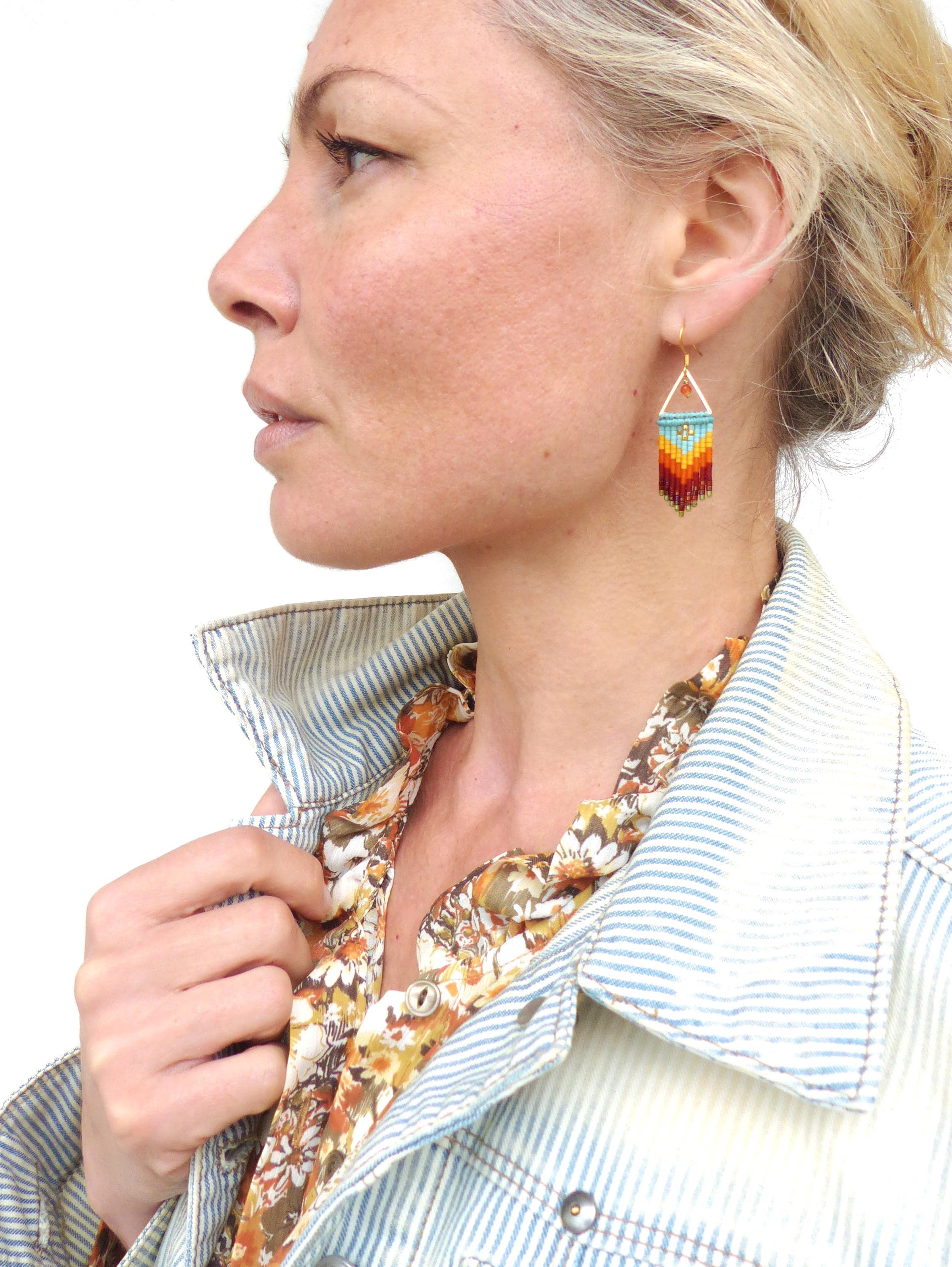 Peut inclure: Une paire de boucles d'oreilles pendantes avec un motif géométrique. Les boucles d'oreilles sont faites de petites perles dans des tons turquoise, orange, rouge et marron. Les perles sont enfilées sur un fil doré et les boucles d'oreilles ont un crochet doré.