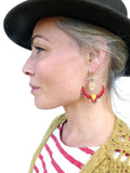 Peut inclure: Une femme portant une chemise à rayures rouges et blanches et un chapeau marron avec une paire de boucles d'oreilles créoles rouges et dorées avec un motif de feuille et des perles colorées.
