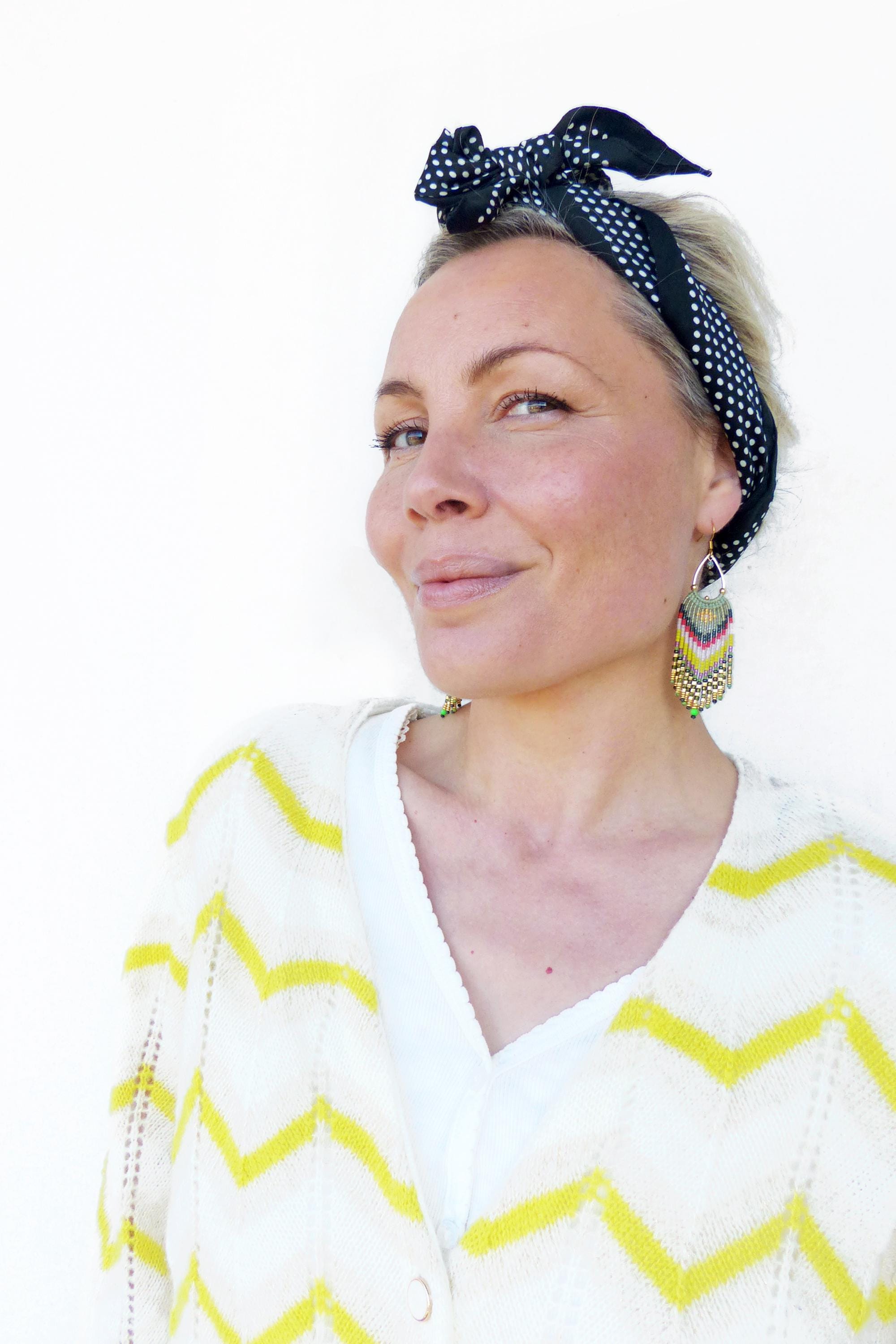 Peut inclure: Une femme portant un cardigan blanc et jaune à chevrons, un bandeau à pois noirs et blancs et de longues boucles d'oreilles en perles. 