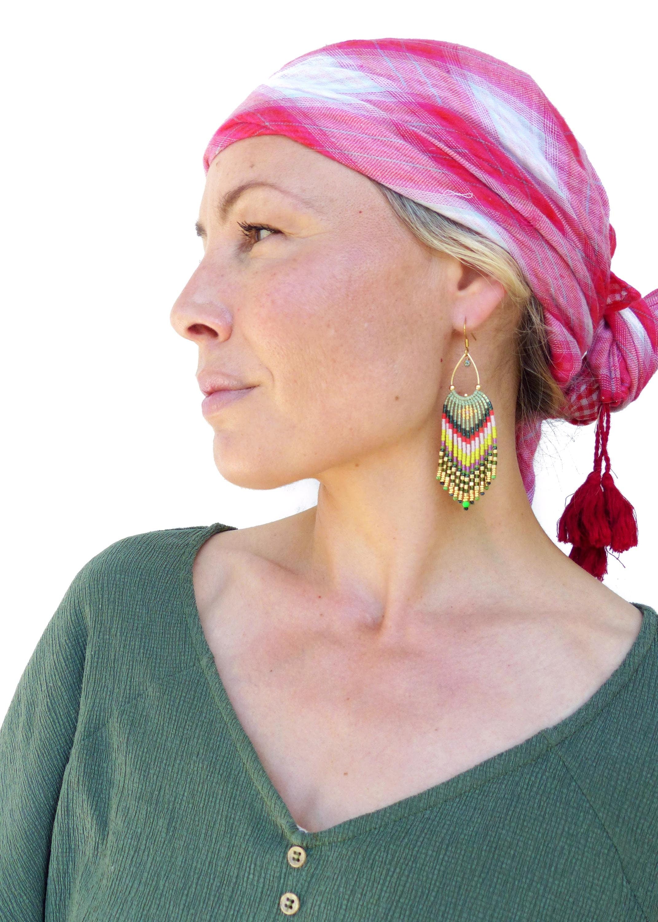 Peut inclure: Une femme portant un foulard à carreaux rouge et blanc avec des glands et une chemise verte à boutons. Elle porte de longues boucles d'oreilles en perles colorées.