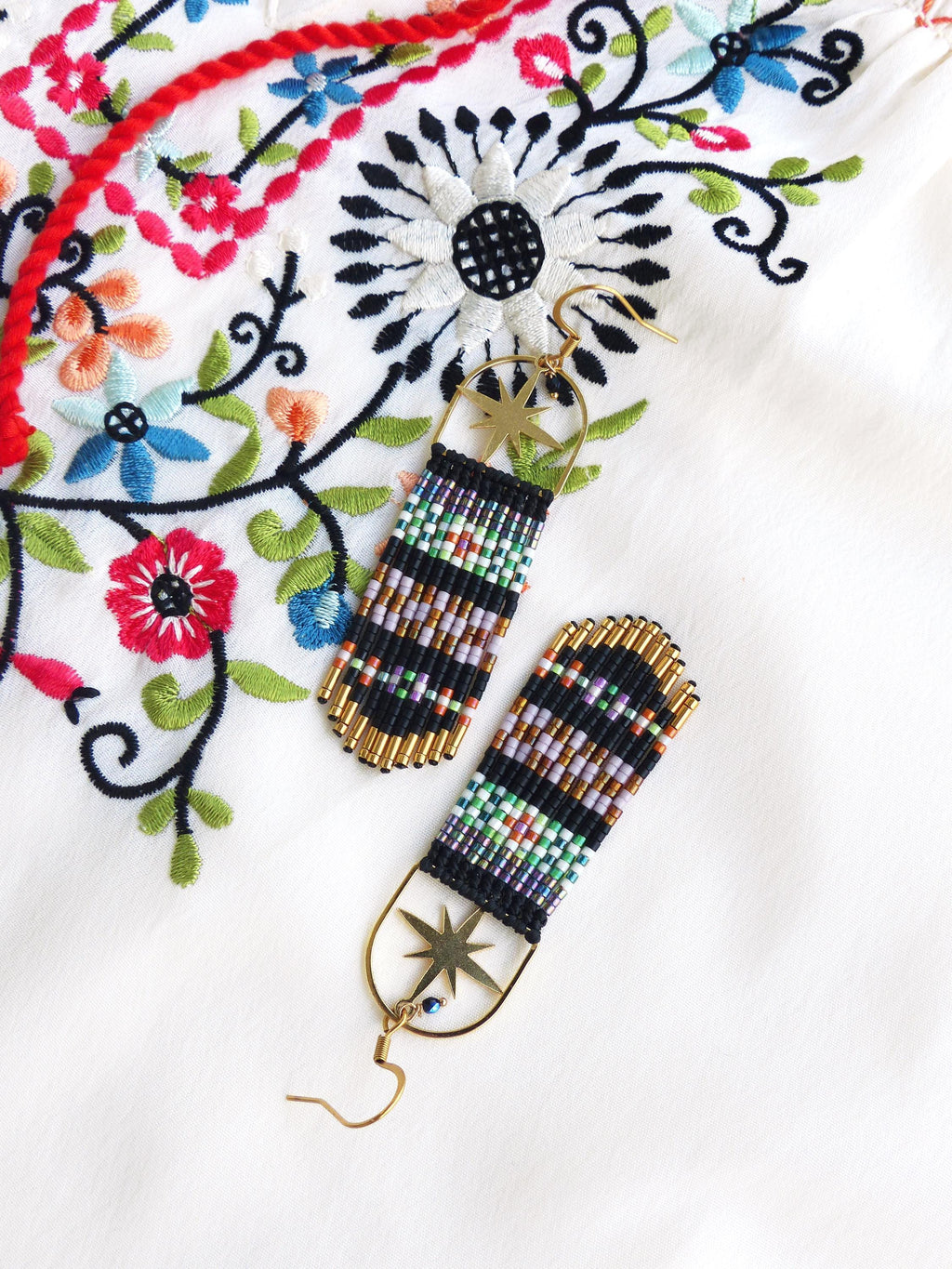 Peut inclure: Une paire de longues boucles d'oreilles en perles avec un charme d'étoile dorée et une perle bleue de mauvais œil. Les boucles d'oreilles sont noires, blanches et multicolores.