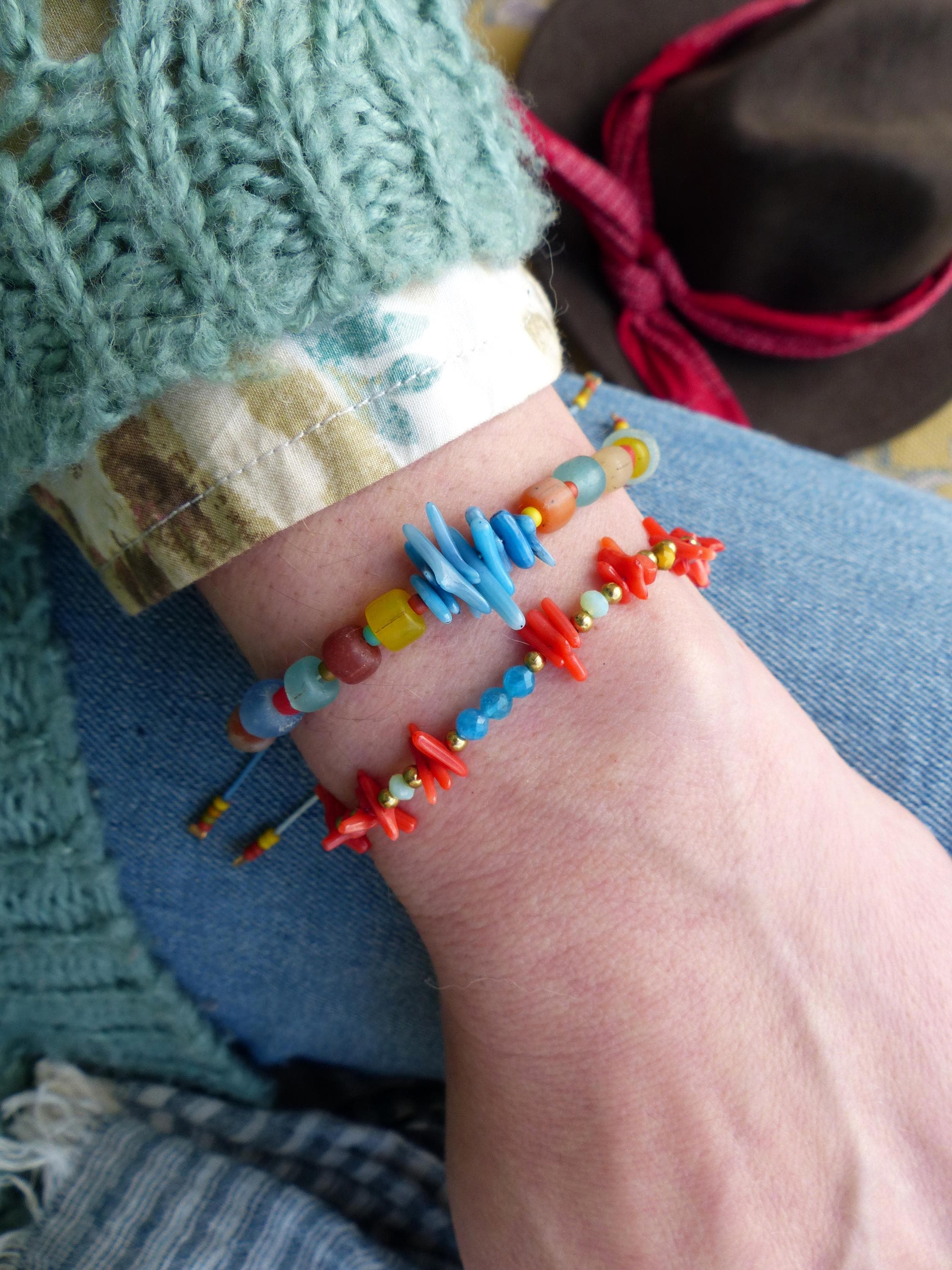 Peut inclure: Deux bracelets avec des perles et des breloques colorées. Un bracelet a des perles bleues, jaunes et rouges, et l'autre a des perles rouges et bleues avec des breloques en forme de corail.