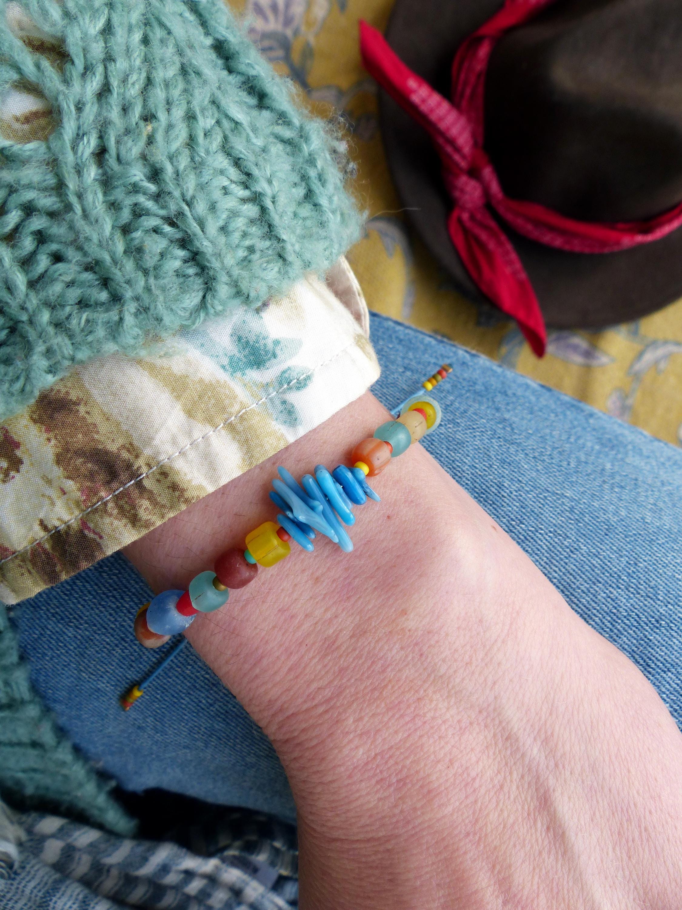 Peut inclure: Un bracelet en perles colorées avec des perles bleues, jaunes, rouges et vertes. Le bracelet est attaché avec un cordon bleu fin et présente un groupe d'éclats de verre bleus au centre.