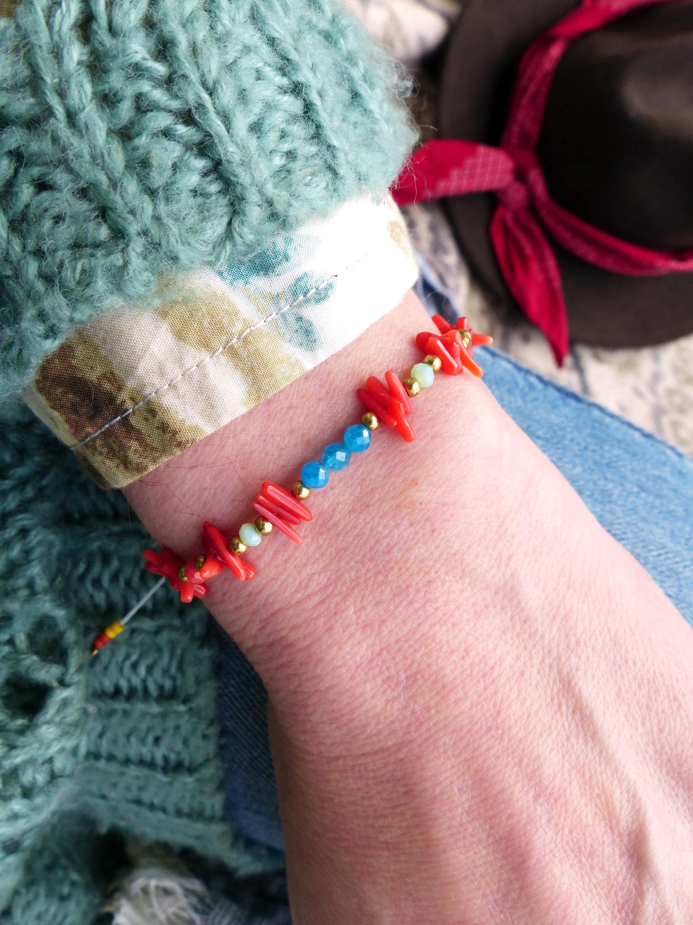 Peut inclure: Un bracelet en perles rouges, corail et bleues avec un design délicat et superposé. Le bracelet est composé de petites pièces irrégulières de corail et de perles de verre bleues.