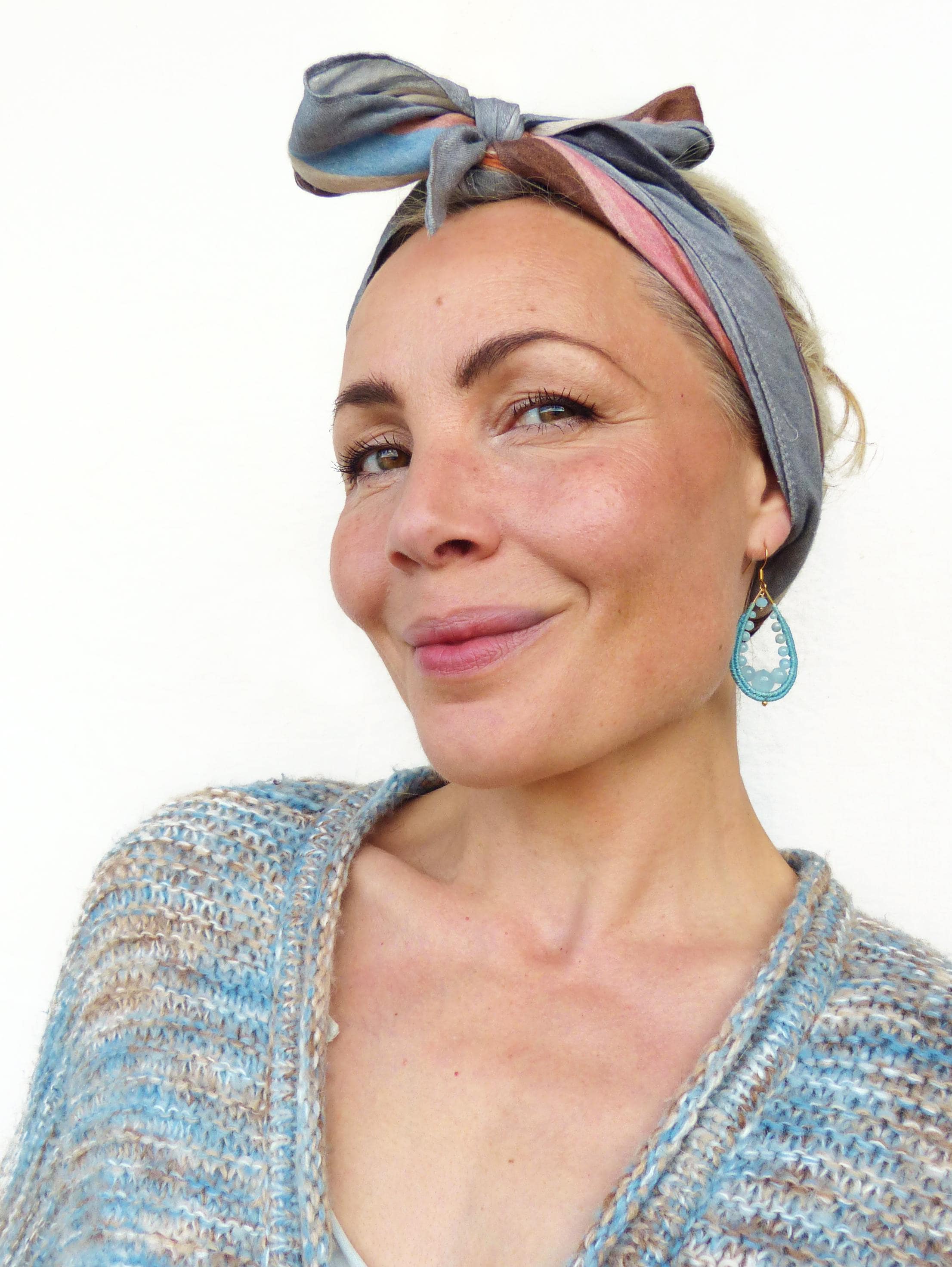Peut inclure: Une femme portant un bandeau à motifs bleu clair et rose et des boucles d'oreilles en forme de larme turquoise. Elle porte un cardigan en tricot bleu clair et marron.