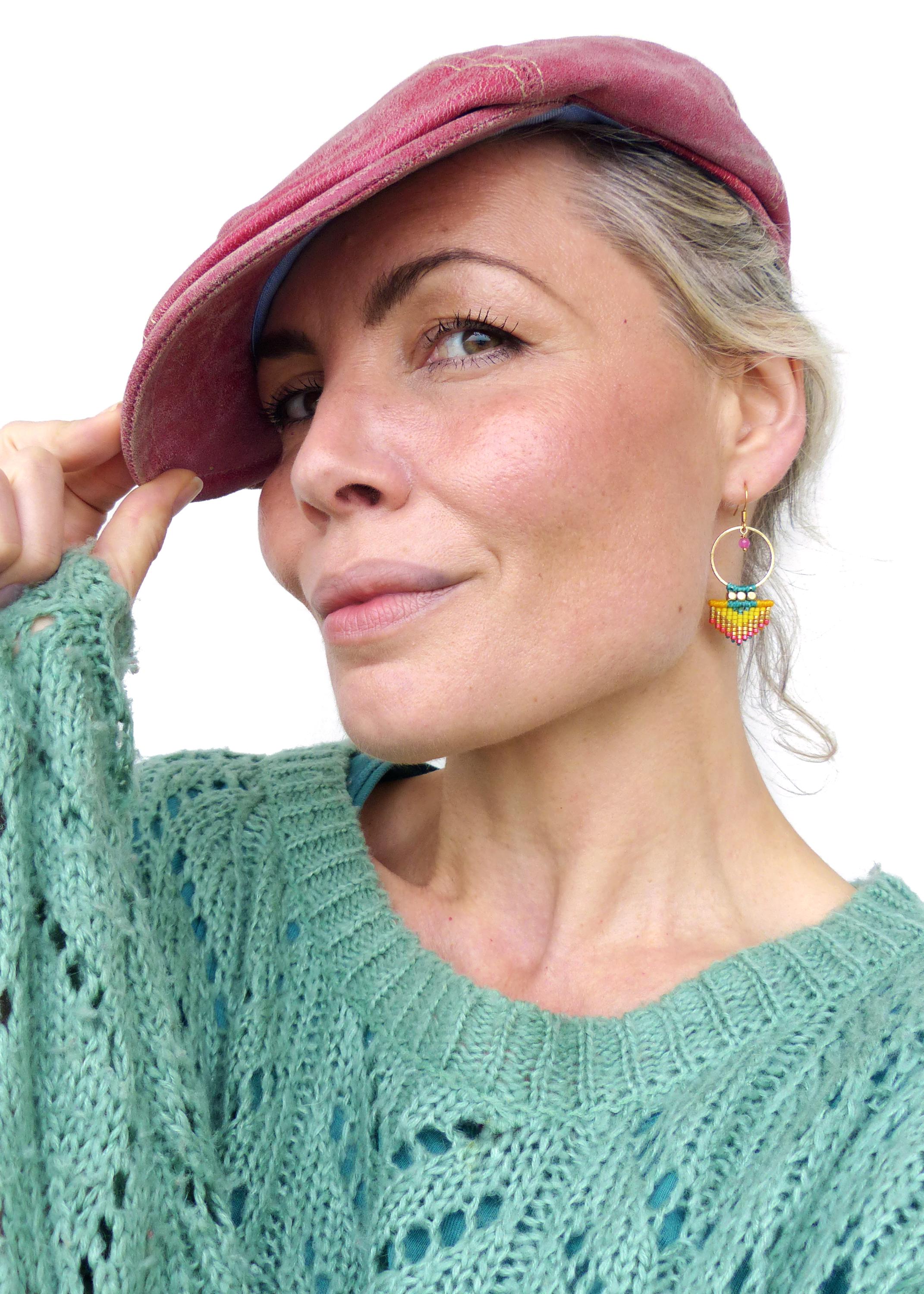 Peut inclure: Une femme porte une casquette rose et un pull vert. Elle porte également des boucles d'oreilles créoles dorées avec des accents de perles colorées jaunes, turquoise et rouges. Les boucles d'oreilles sont un accessoire unique et fait à la main.