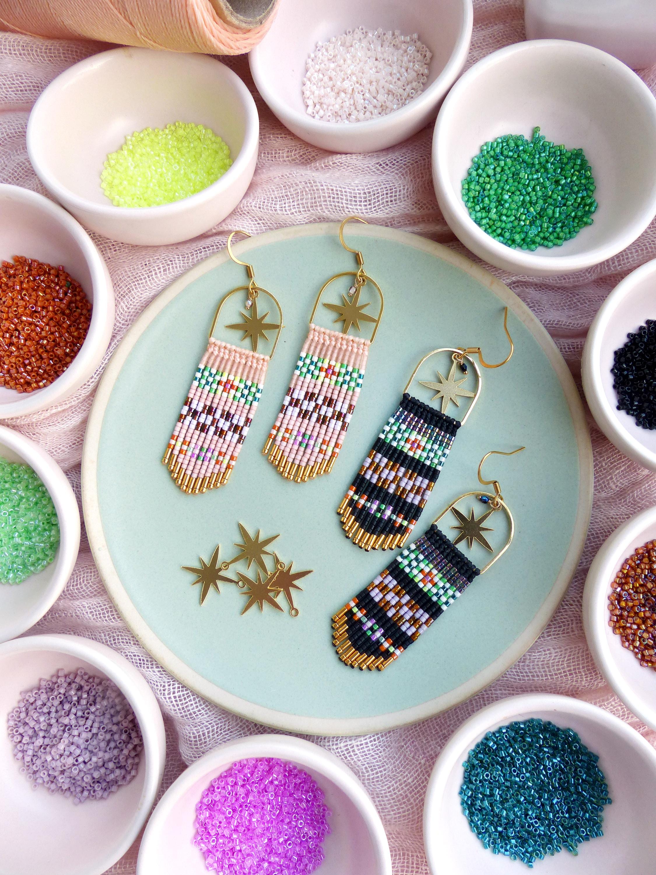 Peut inclure: Une paire de boucles d'oreilles en perles faites à la main avec des breloques d'étoiles dorées. Les boucles d'oreilles sont faites avec des perles de rocaille colorées et ont un design en frange. Les boucles d'oreilles sont présentées sur une assiette bleu clair avec de petits bols de perles qui l'entourent.