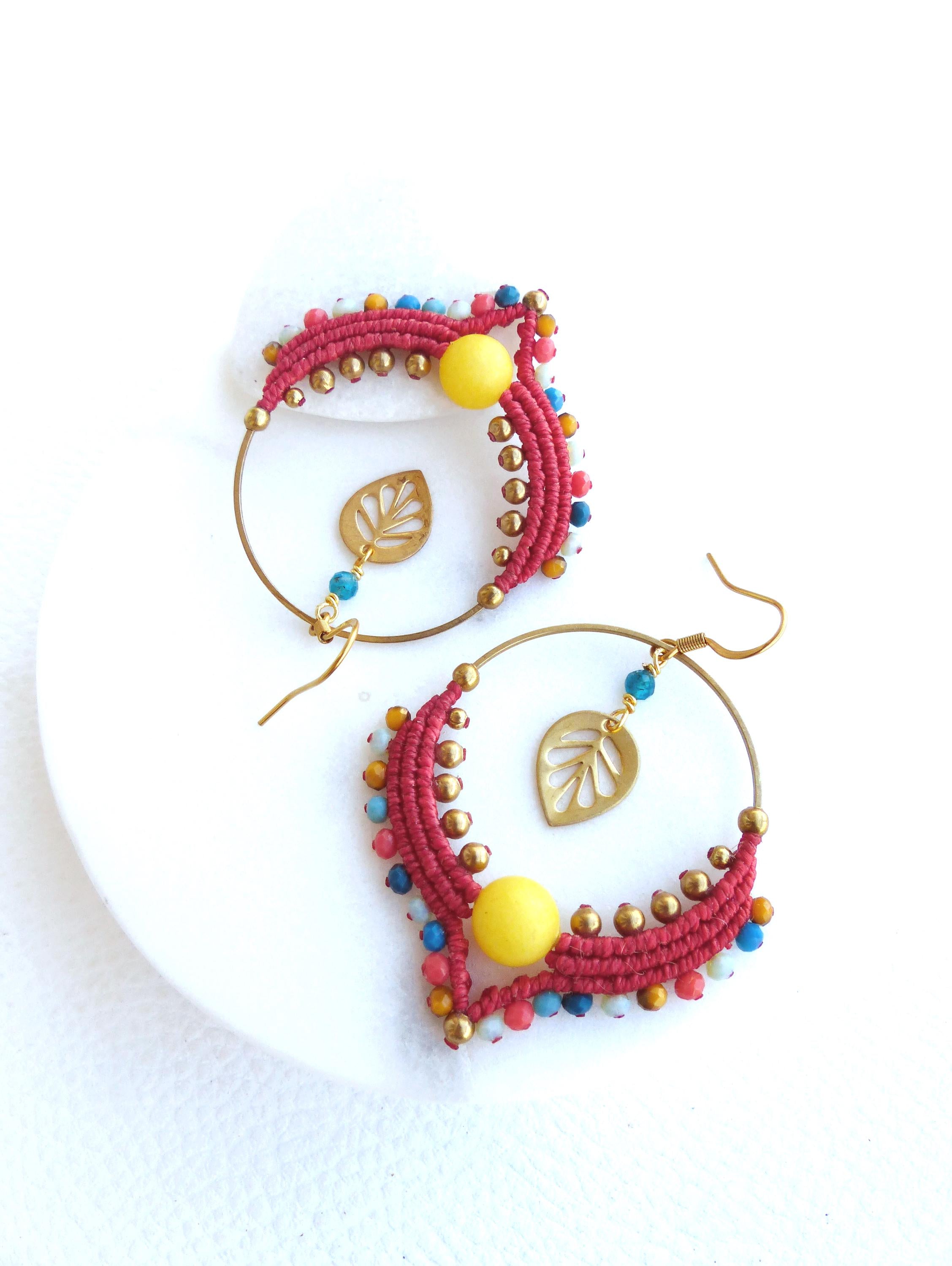 Peut inclure: Une paire de boucles d'oreilles créoles en perles rouges, bleues et jaunes avec un charme en feuille d'or. Les boucles d'oreilles sont faites à la main et ont un style bohème.