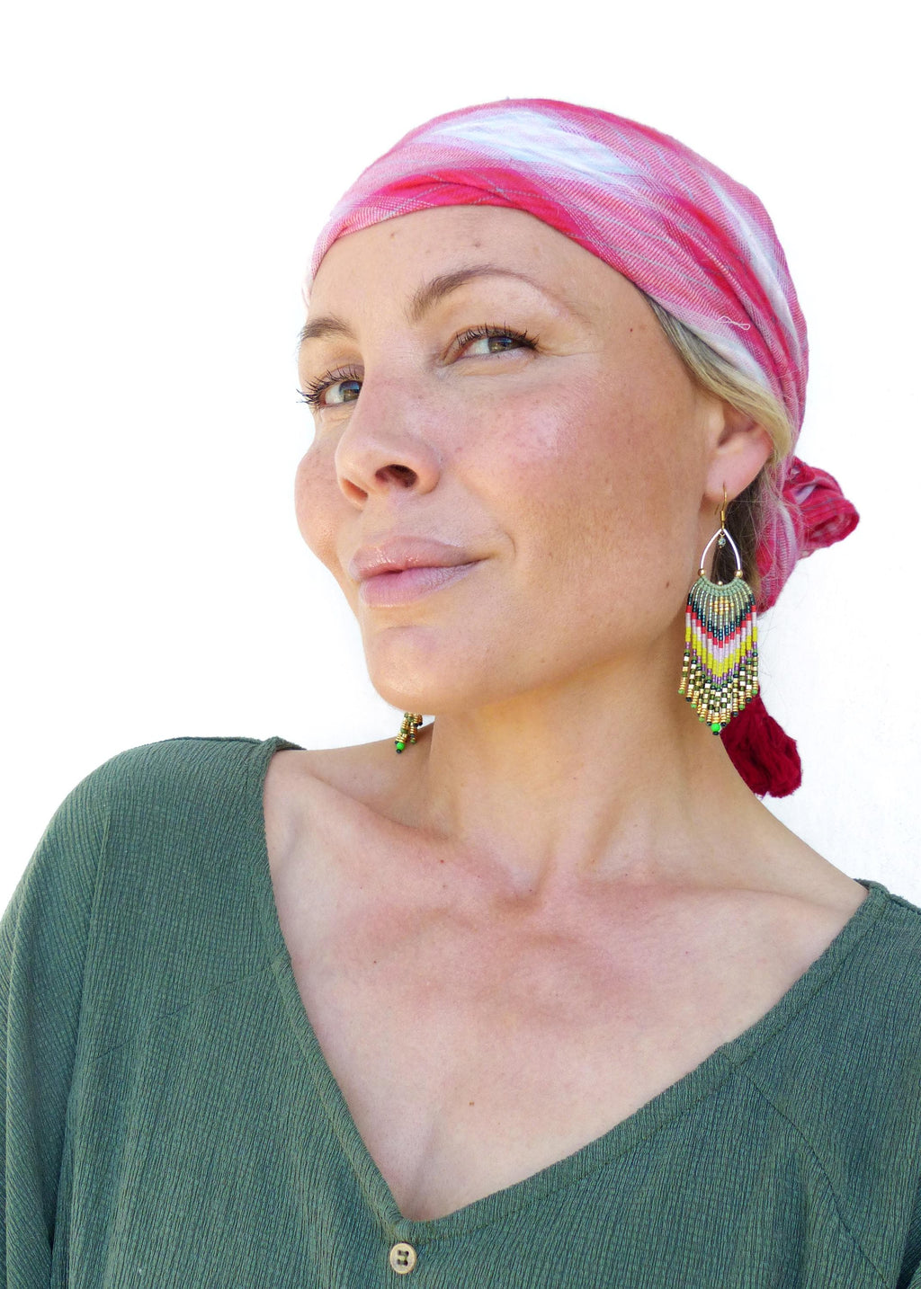 Peut inclure: Une femme portant un foulard à motifs rouge et blanc et une chemise verte. Elle porte de longues boucles d'oreilles en perles avec des accents verts, jaunes et rouges.