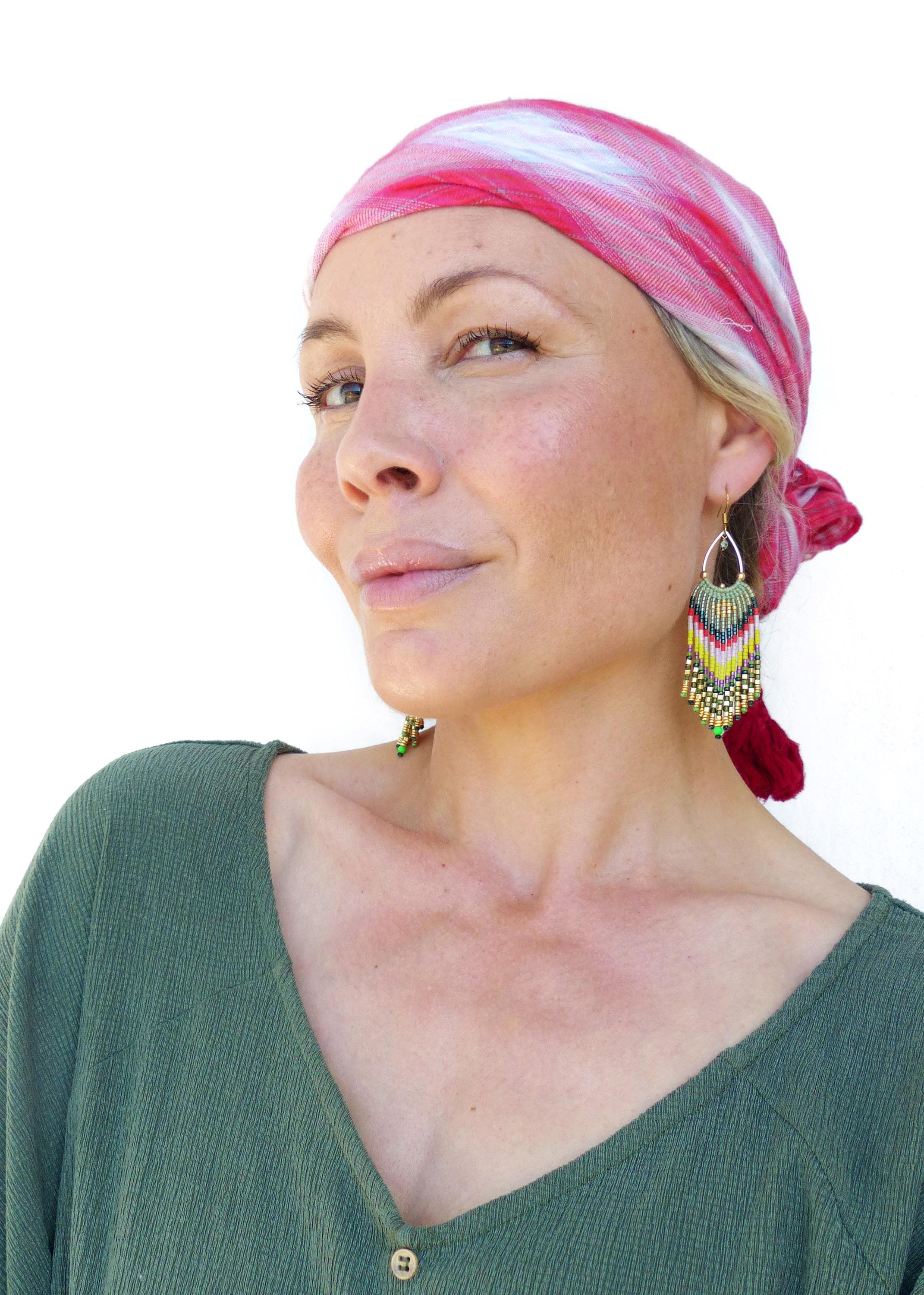 Peut inclure: Une femme portant un foulard à motifs rouge et blanc et une chemise verte. Elle porte de longues boucles d'oreilles en perles avec des accents verts, jaunes et rouges.