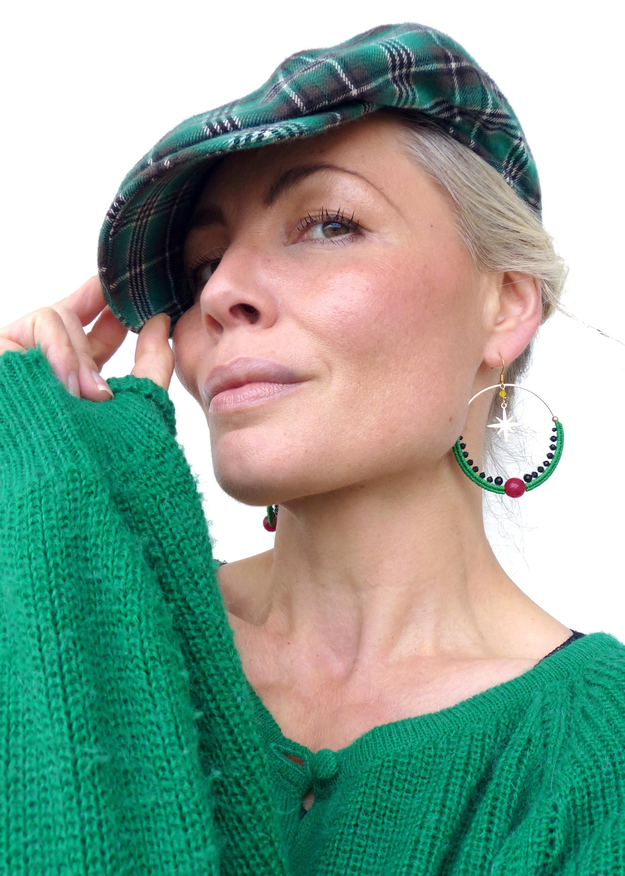 Peut inclure: Une femme porte un béret vert à carreaux et un pull vert en tricot. Elle porte également de grandes boucles d'oreilles créoles avec des détails verts et rouges. Les boucles d'oreilles ont un charme en forme d'étoile.