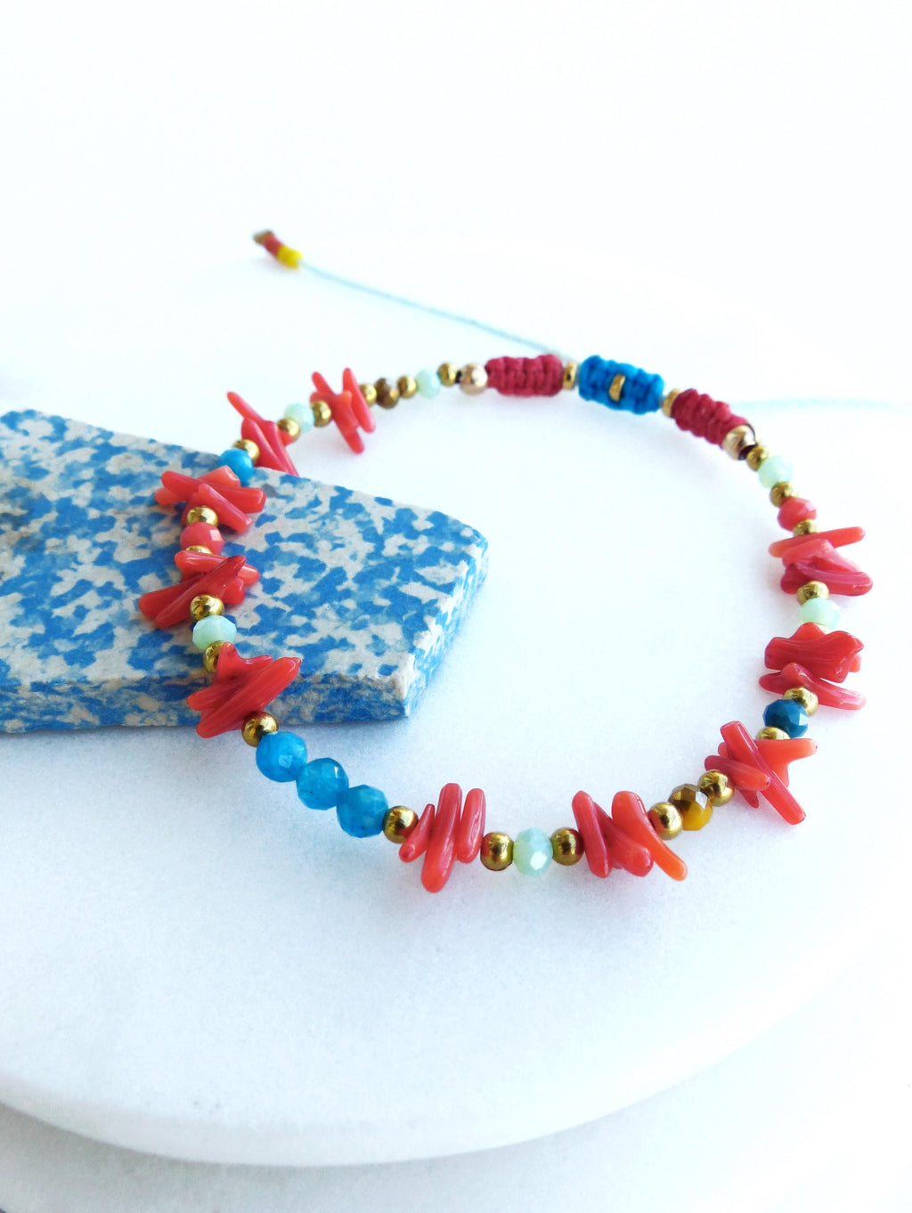 Peut inclure: Un bracelet en perles colorées avec du corail rouge, des pierres bleues et vertes et des accents dorés.
