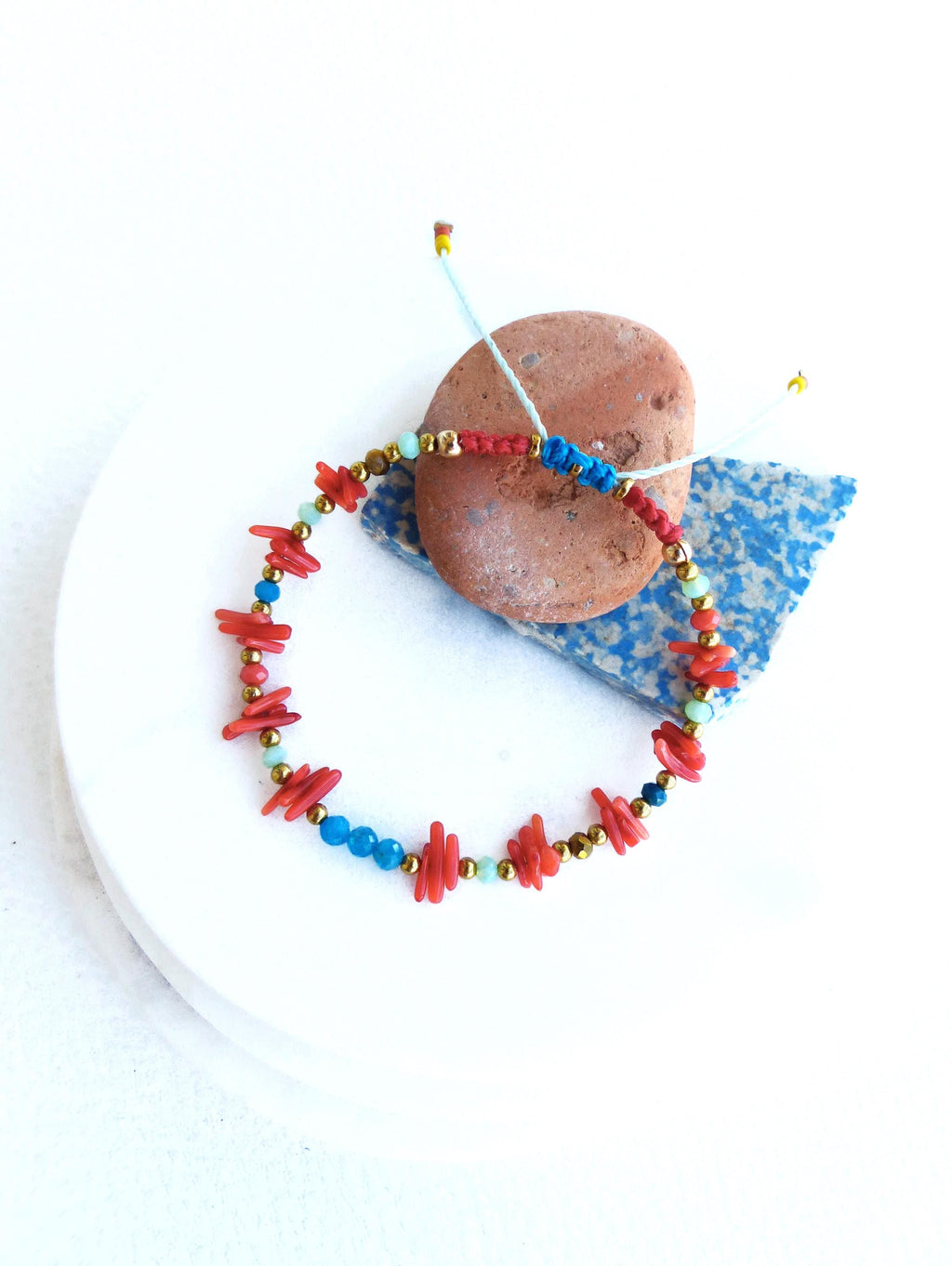 Peut inclure: Un bracelet en perles rouges et bleues avec des accents dorés. Le bracelet est composé de petites perles rouges plates et de perles bleues rondes. Le bracelet est noué avec un cordon bleu clair.