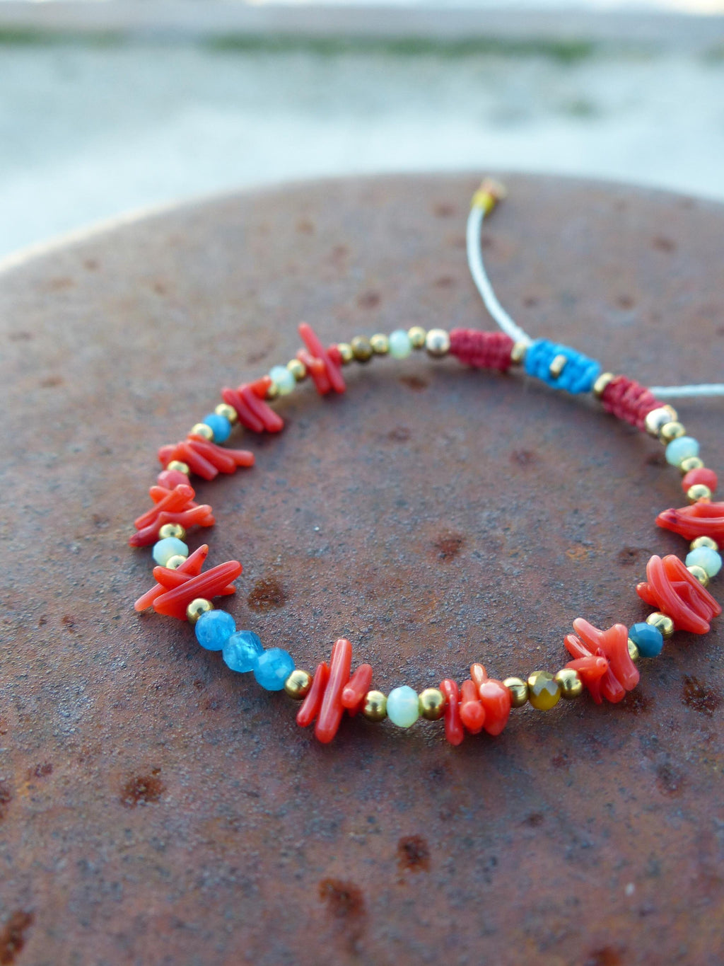 Peut inclure: Un bracelet en perles de corail rouge et turquoise avec des accents dorés. Le bracelet est composé de petites perles de corail et de turquoise irrégulières, entrecoupées de perles dorées.