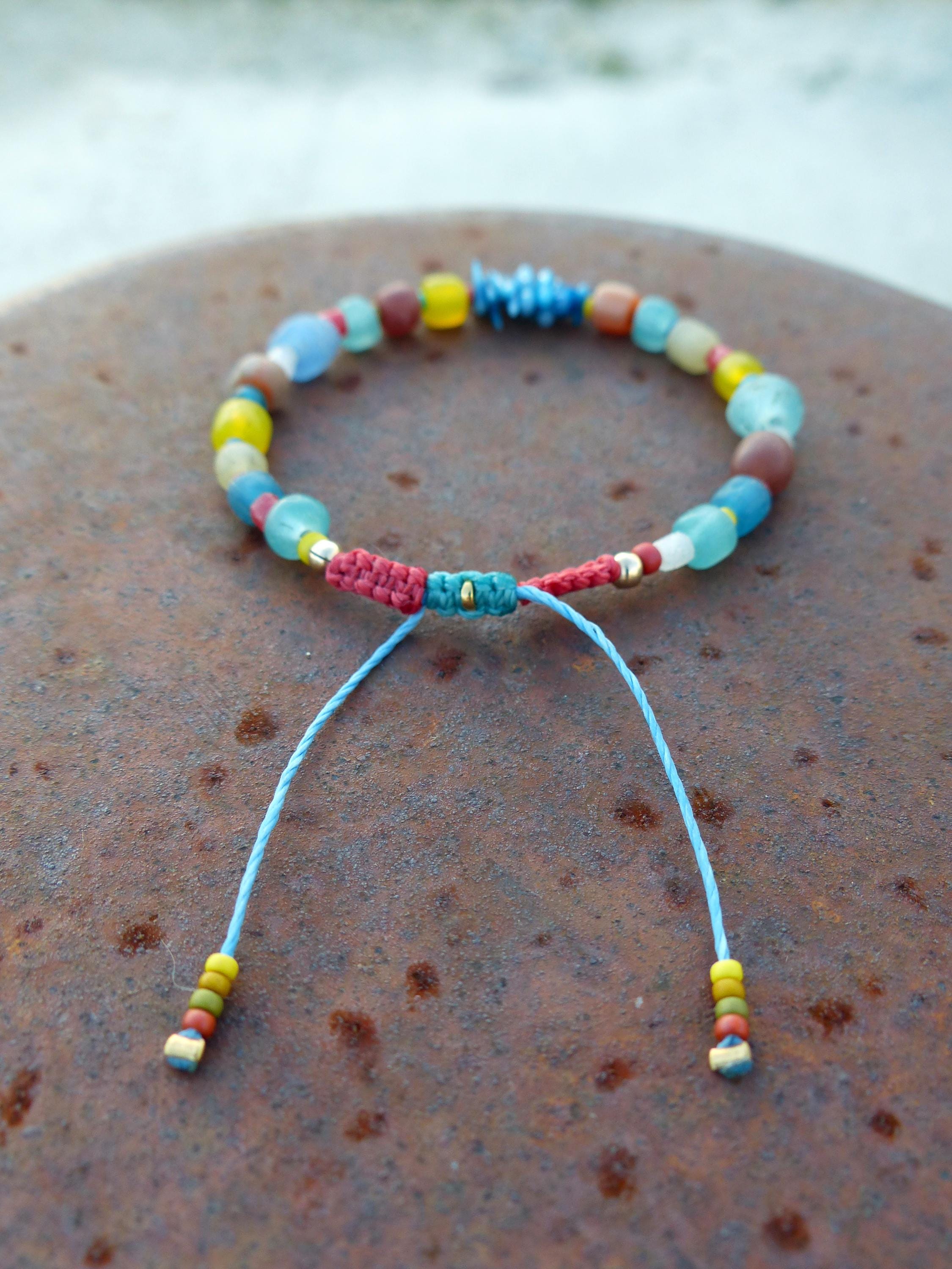 Peut inclure: Un bracelet en perles colorées avec un cordon rouge, bleu et vert. Les perles sont en verre et sont dans des tons de bleu, vert, jaune et marron.