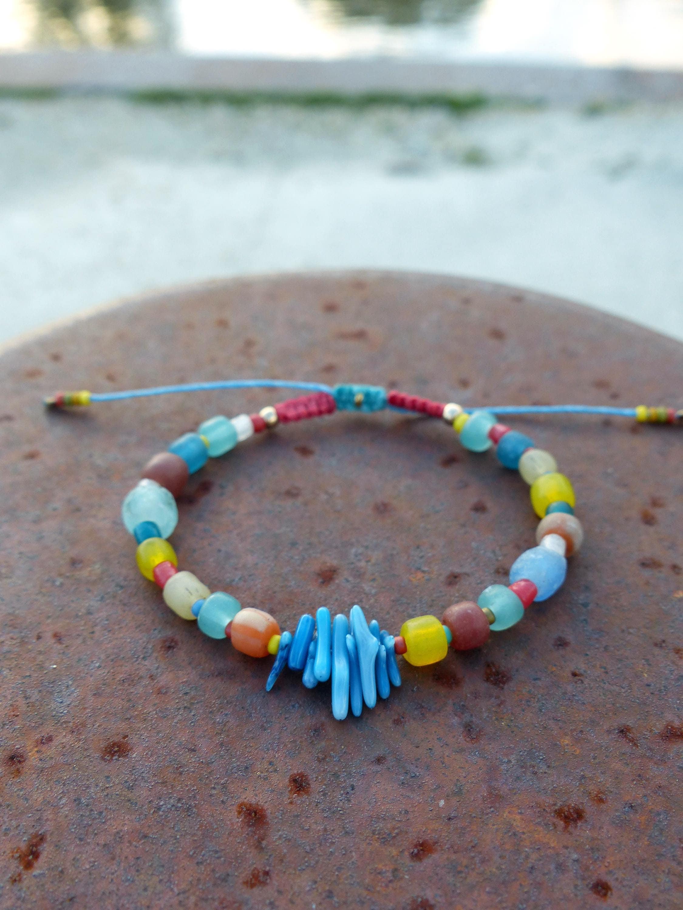 Peut inclure: Un bracelet en perles colorées avec un charme en corail bleu. Le bracelet est composé de perles de verre de différentes couleurs, bleu, vert, jaune, rouge et orange. Les perles sont enfilées sur un cordon bleu et nouées.
