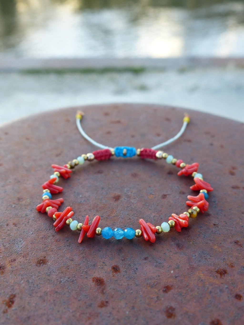 Peut inclure: Un bracelet en corail rouge et pierres bleues avec des perles dorées et un cordon blanc.