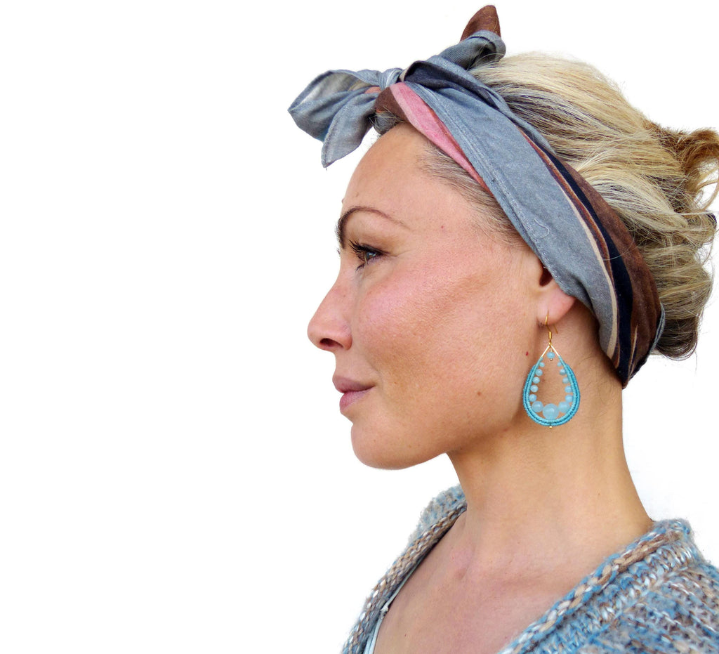 Peut inclure: Une femme aux cheveux blonds portant un bandana rayé bleu et marron et des boucles d'oreilles en perles turquoise. 