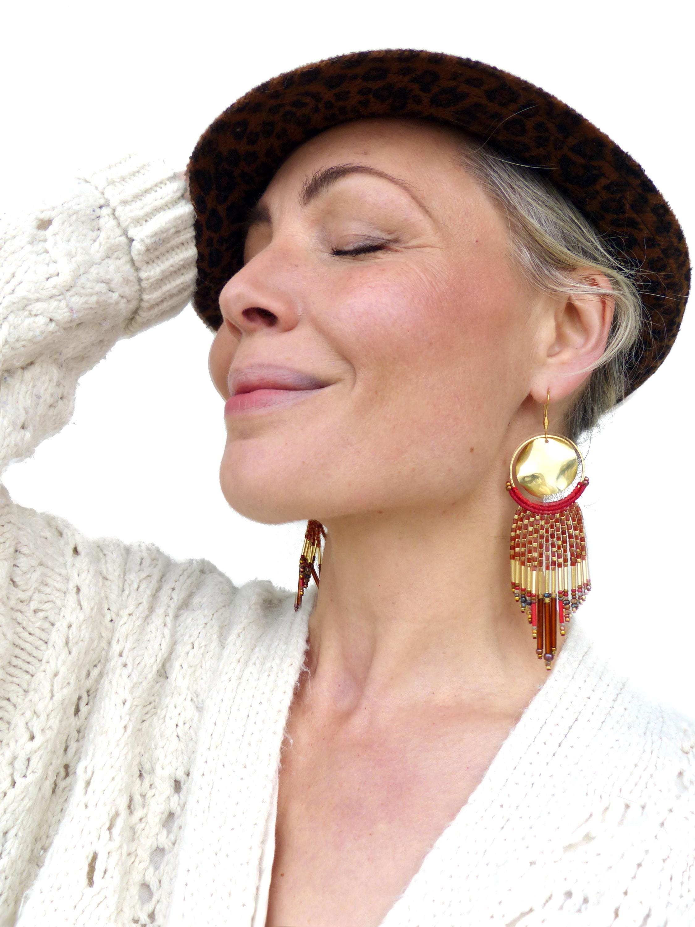 Peut inclure: Une femme portant un pull blanc et un chapeau léopard marron avec de longues boucles d'oreilles en perles avec des accents dorés et rouges.