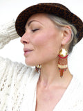 Peut inclure: Une femme portant un chapeau léopard brun et noir et un pull en tricot blanc à manches longues. Elle porte de longues boucles d'oreilles pendantes avec des perles dorées et rouges.