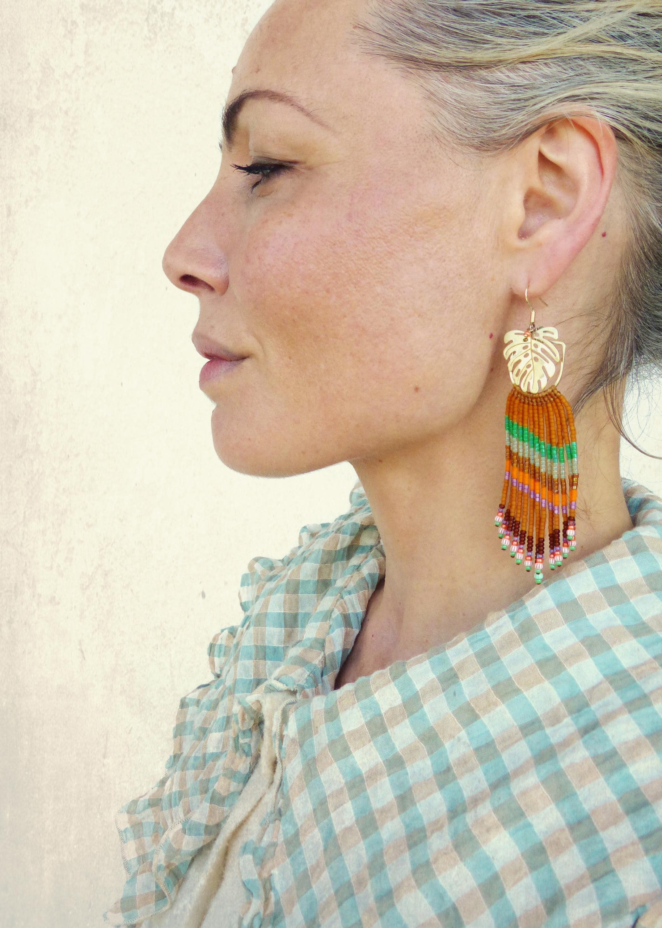 Peut inclure: Boucles d'oreilles dorées en forme de feuille avec une frange de perles aux tons orange, vert et rose. Les boucles d'oreilles sont longues et pendantes, ajoutant une touche bohème. Un accessoire unique.