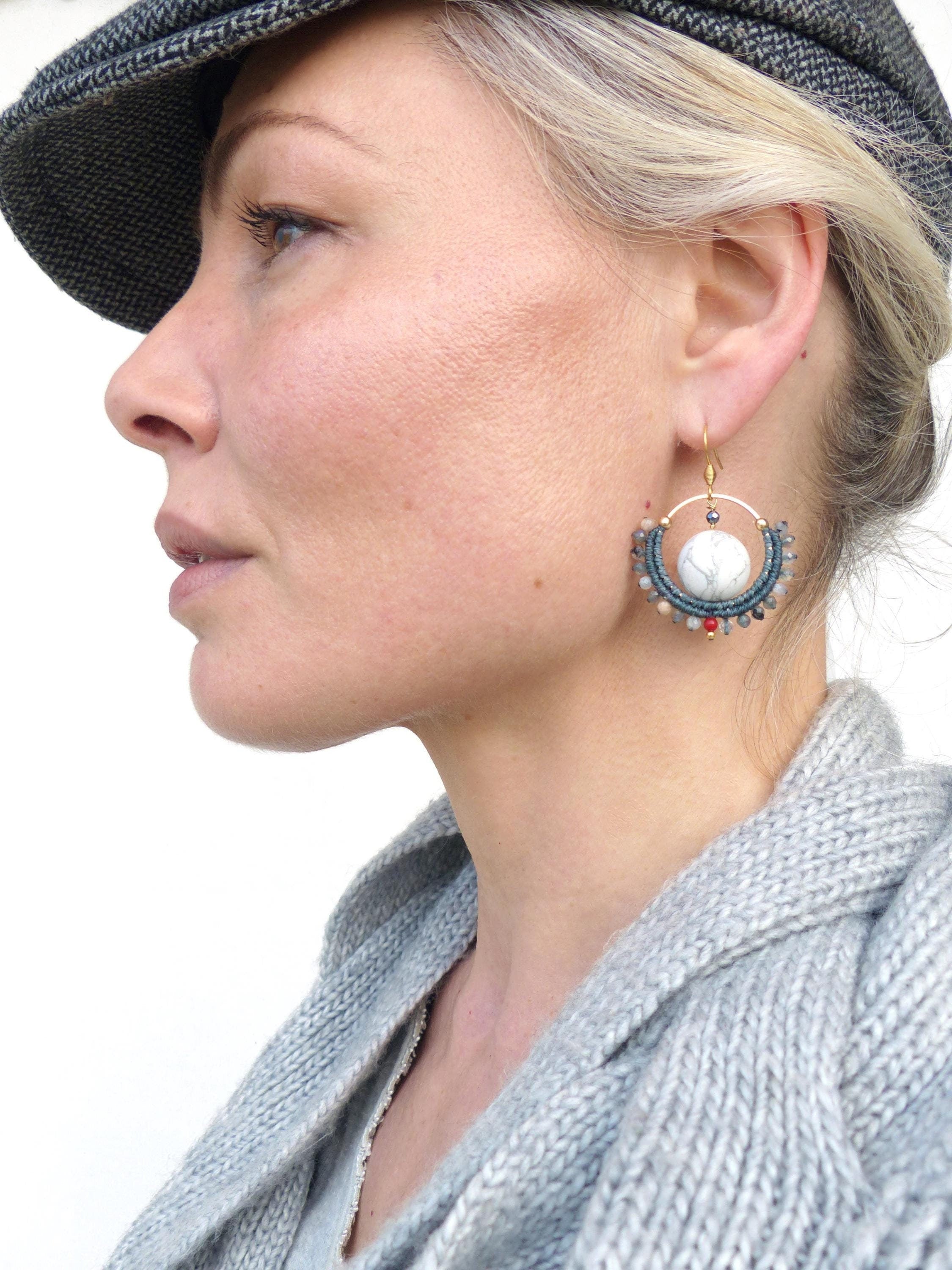 Peut inclure: Boucles d'oreilles dorées avec un centre en pierre blanche et un anneau extérieur perlé dans les tons de bleu, gris et rouge. Les boucles d'oreilles sont suspendues à un crochet doré. Un accessoire unique.