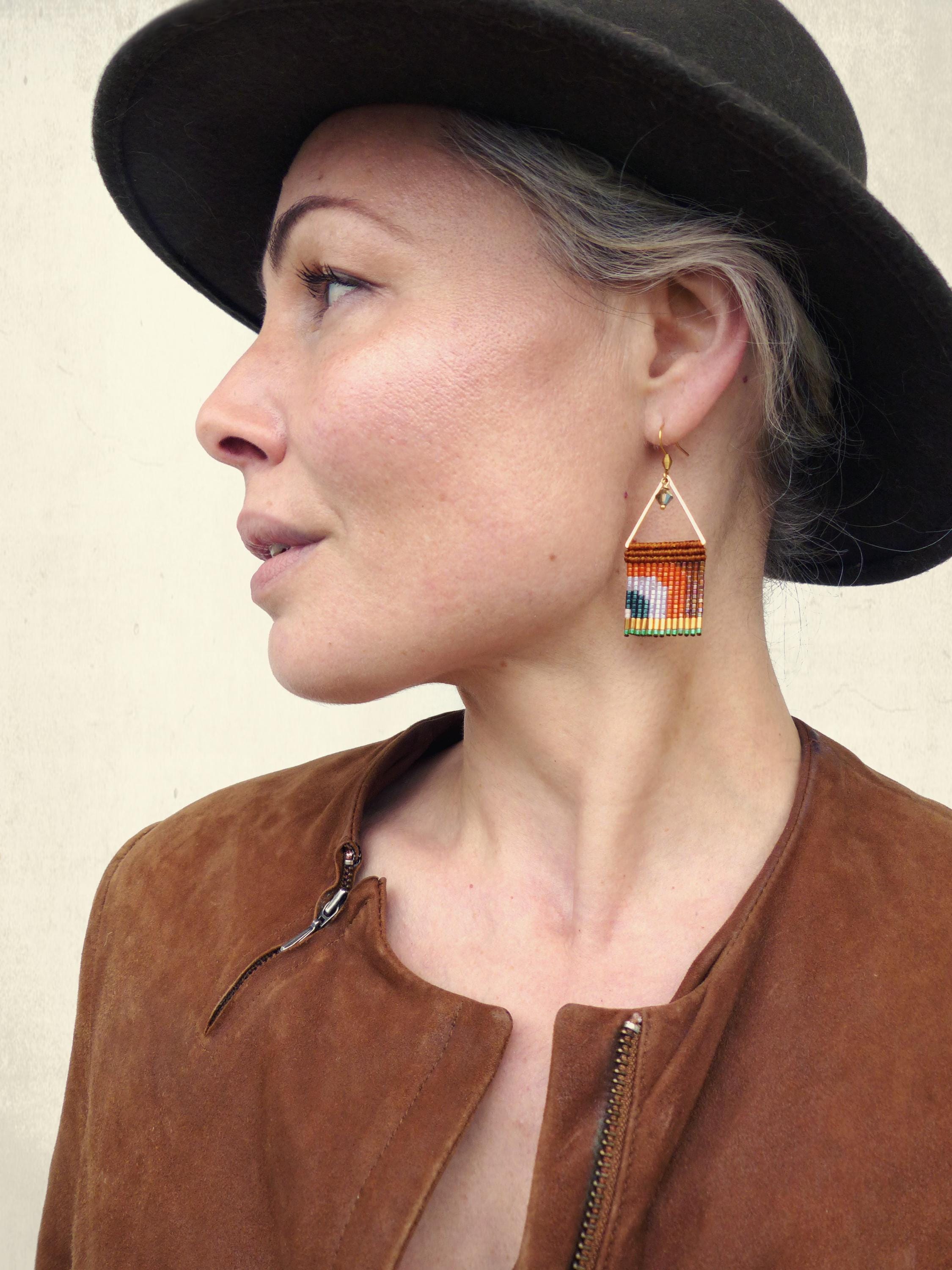 Peut inclure: Boucles d'oreilles en perles faites à la main avec un motif géométrique. Les boucles d'oreilles ont une forme triangulaire avec un cadre doré et un motif coloré de perles orange, jaunes, vertes et bleues. Elles sont suspendues à des crochets d'oreilles dorés.