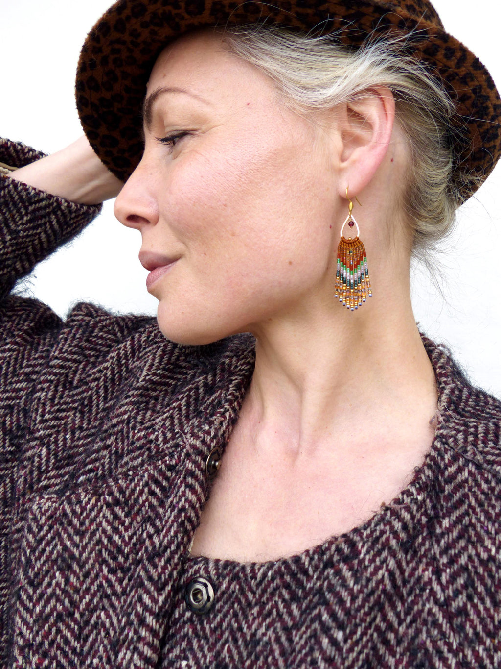 Peut inclure: Une paire de longues boucles d'oreilles en perles de forme larme. Les boucles d'oreilles sont faites de perles brunes, orange, blanches et vertes. Les boucles d'oreilles sont suspendues à des crochets dorés.