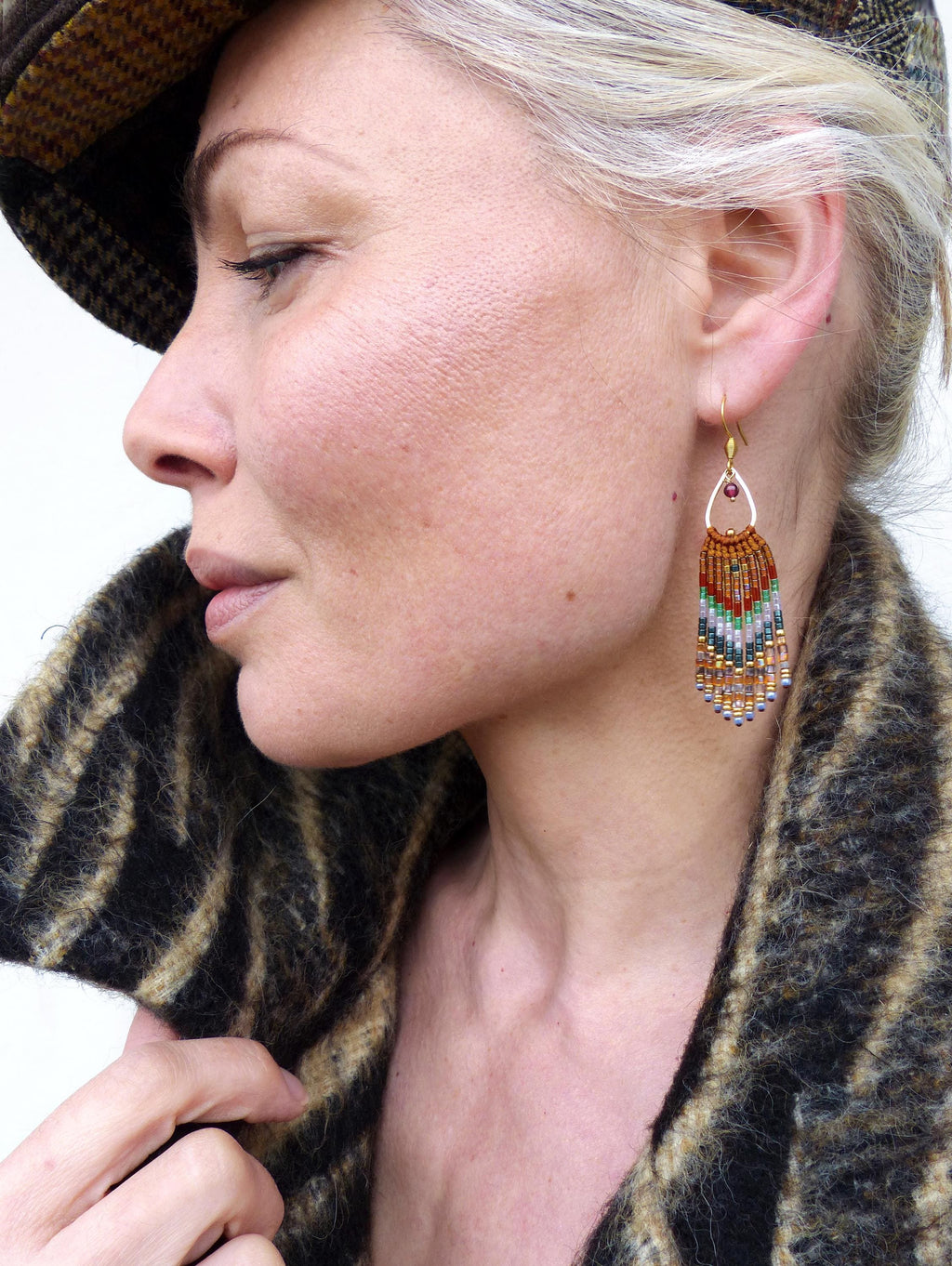 Peut inclure: Une paire de longues boucles d'oreilles en perles avec un motif géométrique dans des tons de brun, vert et blanc. Les boucles d'oreilles sont suspendues à des crochets dorés.