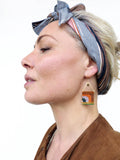Peut inclure: Boucles d'oreilles perlées faites à la main avec un motif géométrique. Les boucles d'oreilles présentent un dessus triangulaire doré et un bas rectangulaire avec des perles orange, vertes et blanches. Elles sont suspendues à des crochets d'oreilles dorés.