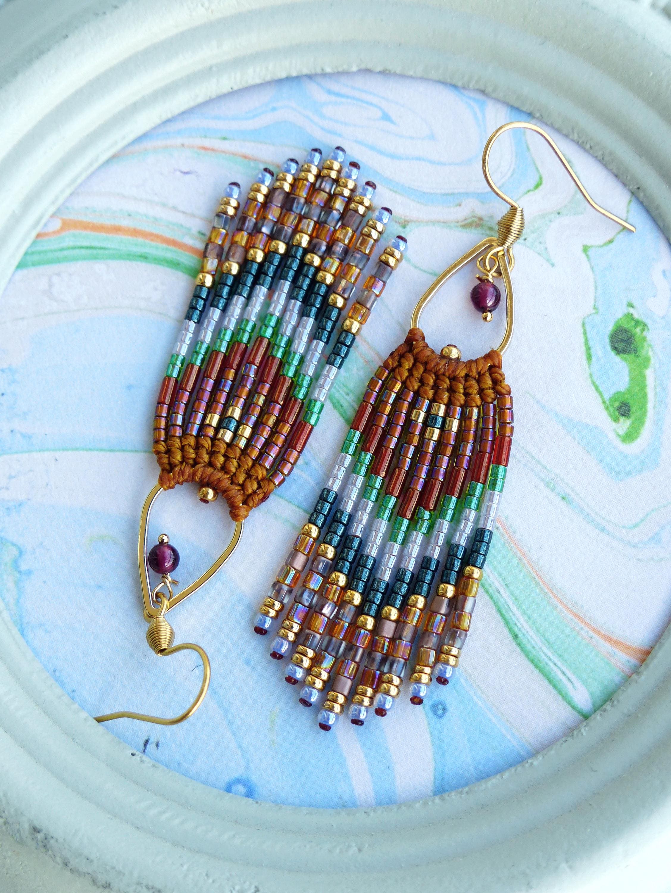 Peut inclure: Une paire de longues boucles d'oreilles pendantes en perles avec un schéma de couleurs brun, or, vert et violet. Les boucles d'oreilles ont un design en forme de larme avec une petite pierre précieuse violette foncée en haut.