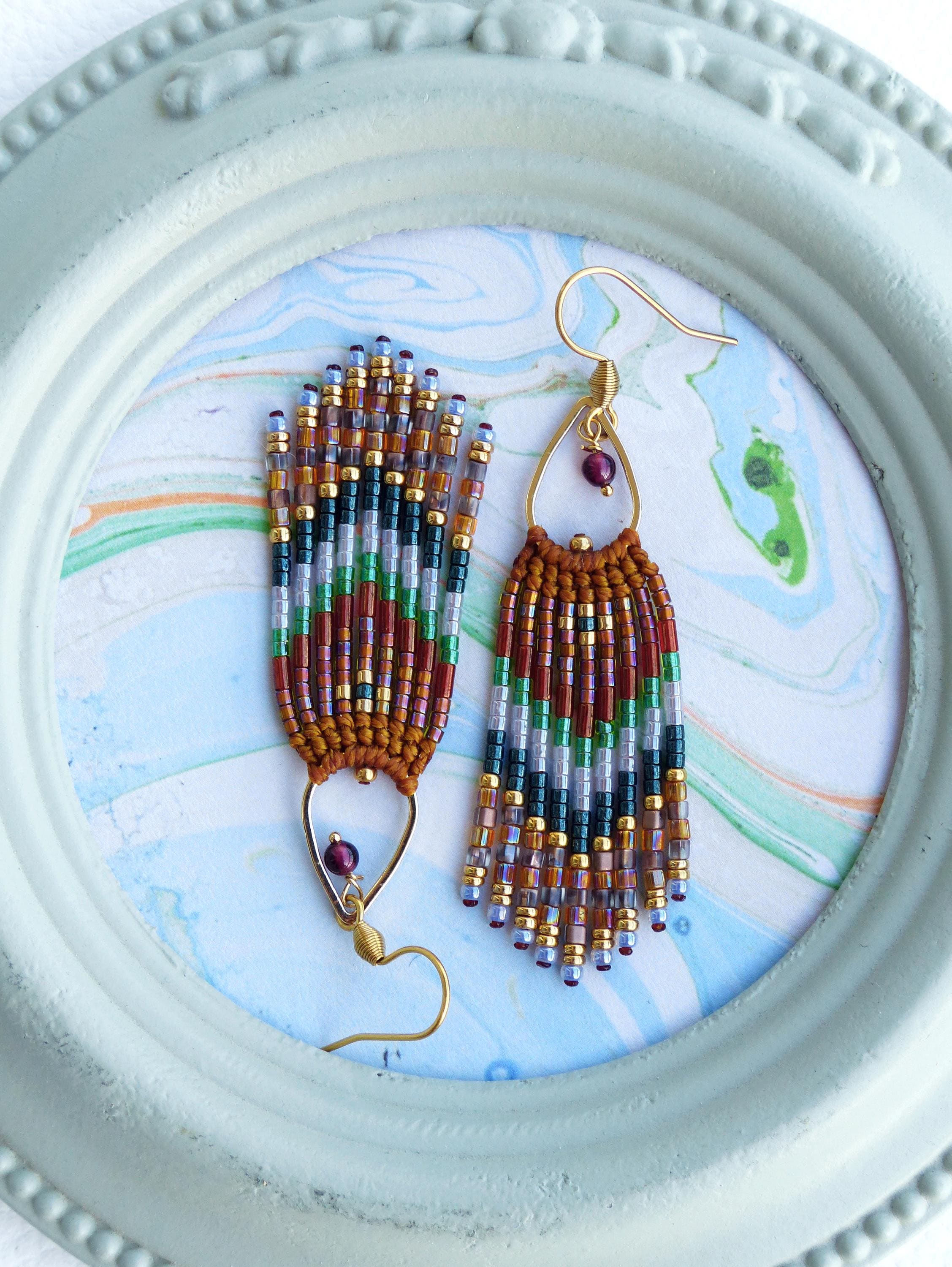 Peut inclure: Une paire de boucles d'oreilles pendantes en perles avec un crochet doré et une perle marron au sommet. Les boucles d'oreilles sont faites de perles brunes, rouges, vertes et dorées.