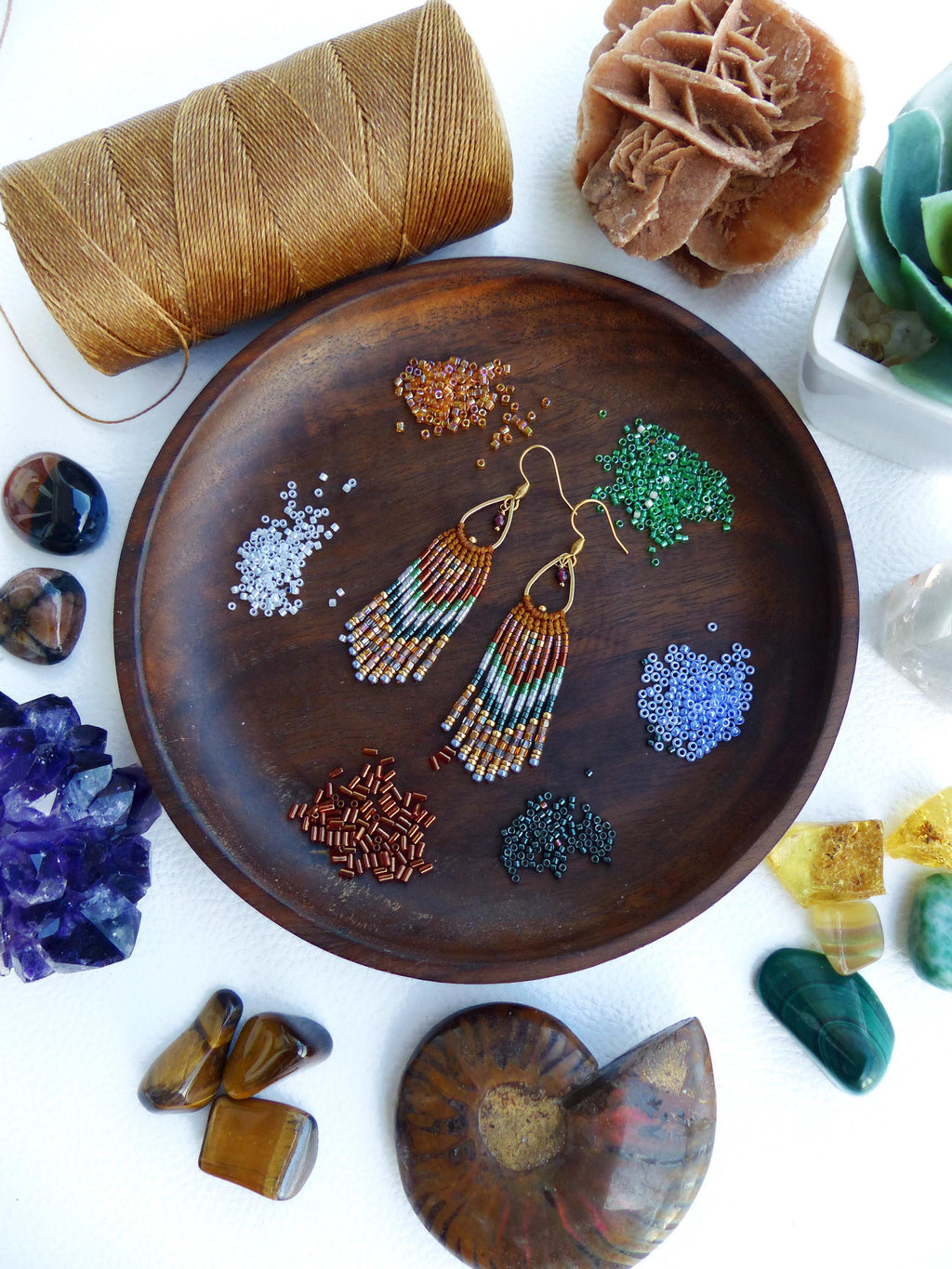 Peut inclure: Un bol en bois rempli de perles et de fournitures pour la fabrication de boucles d'oreilles. Les boucles d'oreilles sont faites de perles colorées et ont un design en frange. Le bol est entouré de diverses pierres et cristaux.