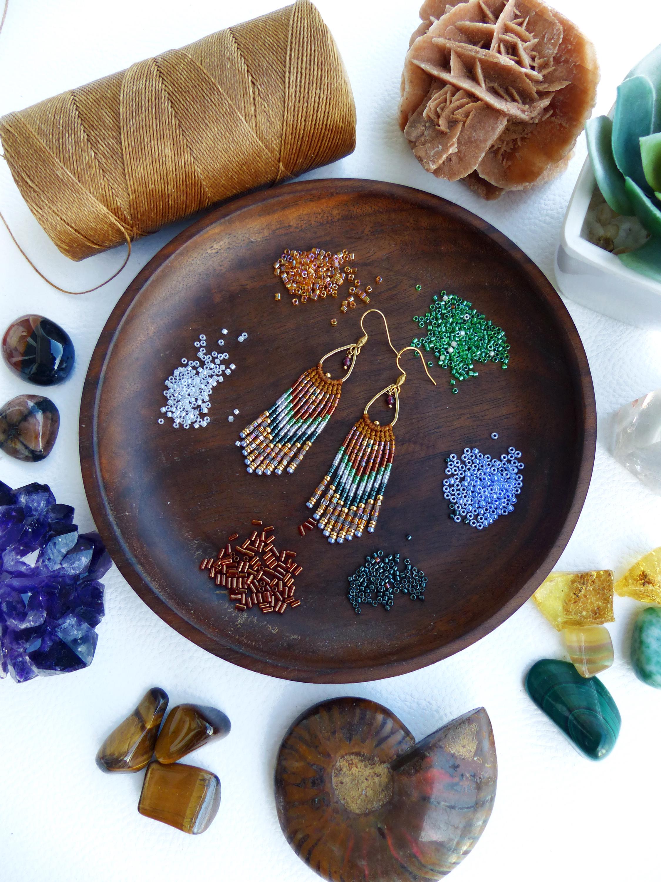 Peut inclure: Un bol en bois rempli de perles et de fournitures pour la fabrication de boucles d'oreilles. Les boucles d'oreilles sont faites de perles colorées et ont un design en frange. Le bol est entouré de diverses pierres et cristaux.