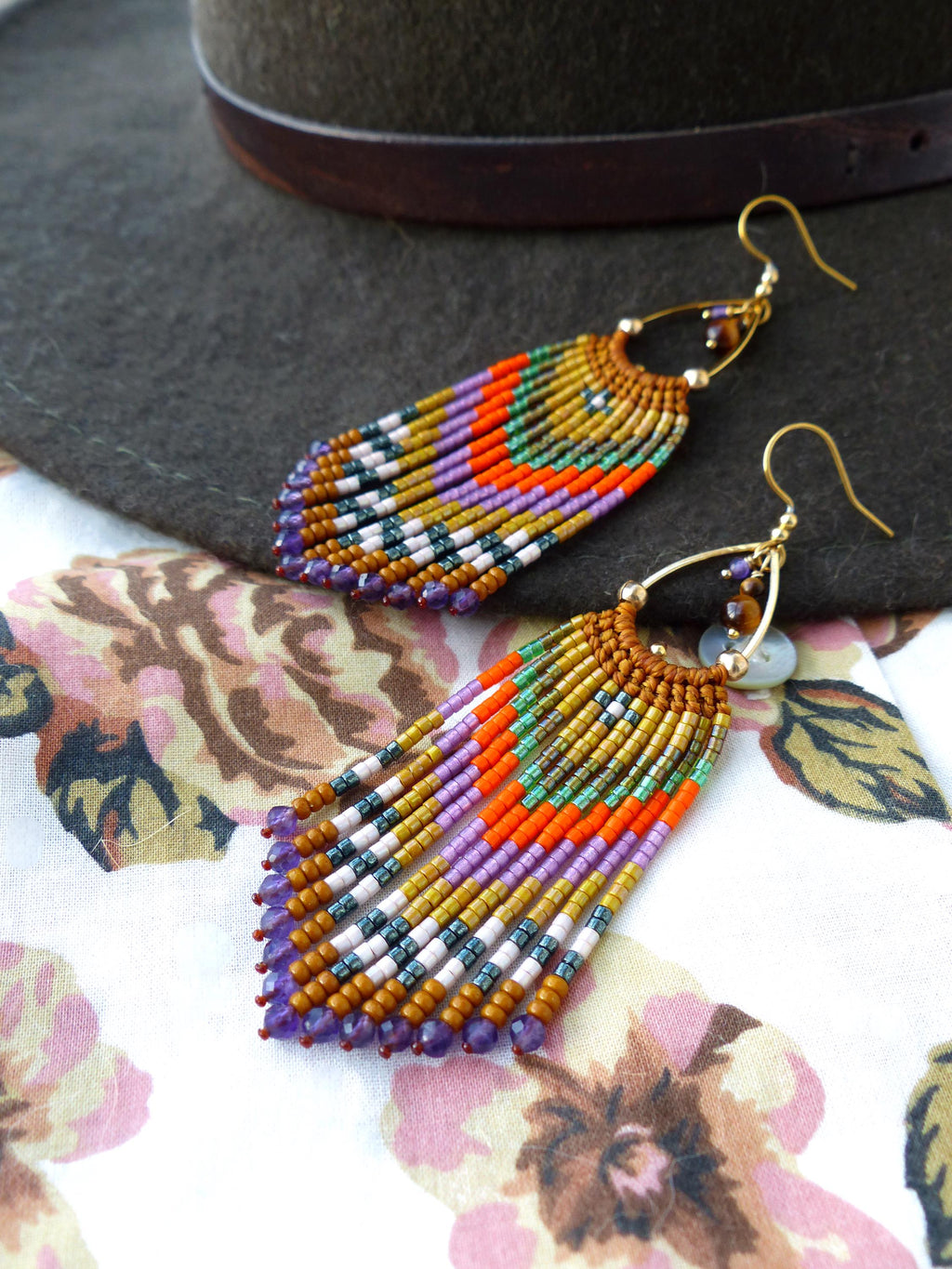 Peut inclure: Une paire de longues boucles d'oreilles en perles colorées avec un design en frange. Les boucles d'oreilles sont faites avec une variété de perles, y compris des améthystes, de l'or et des perles orange. Les boucles d'oreilles sont suspendues à des crochets dorés.