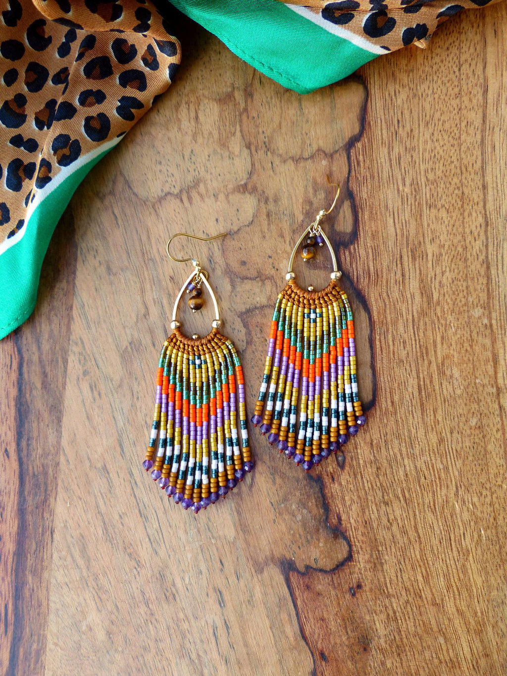 Peut inclure: Une paire de longues boucles d'oreilles pendantes en perles avec un crochet en métal doré. Les boucles d'oreilles sont faites avec une variété de perles colorées, notamment orange, violet, vert et or. Les perles sont disposées selon un motif géométrique.