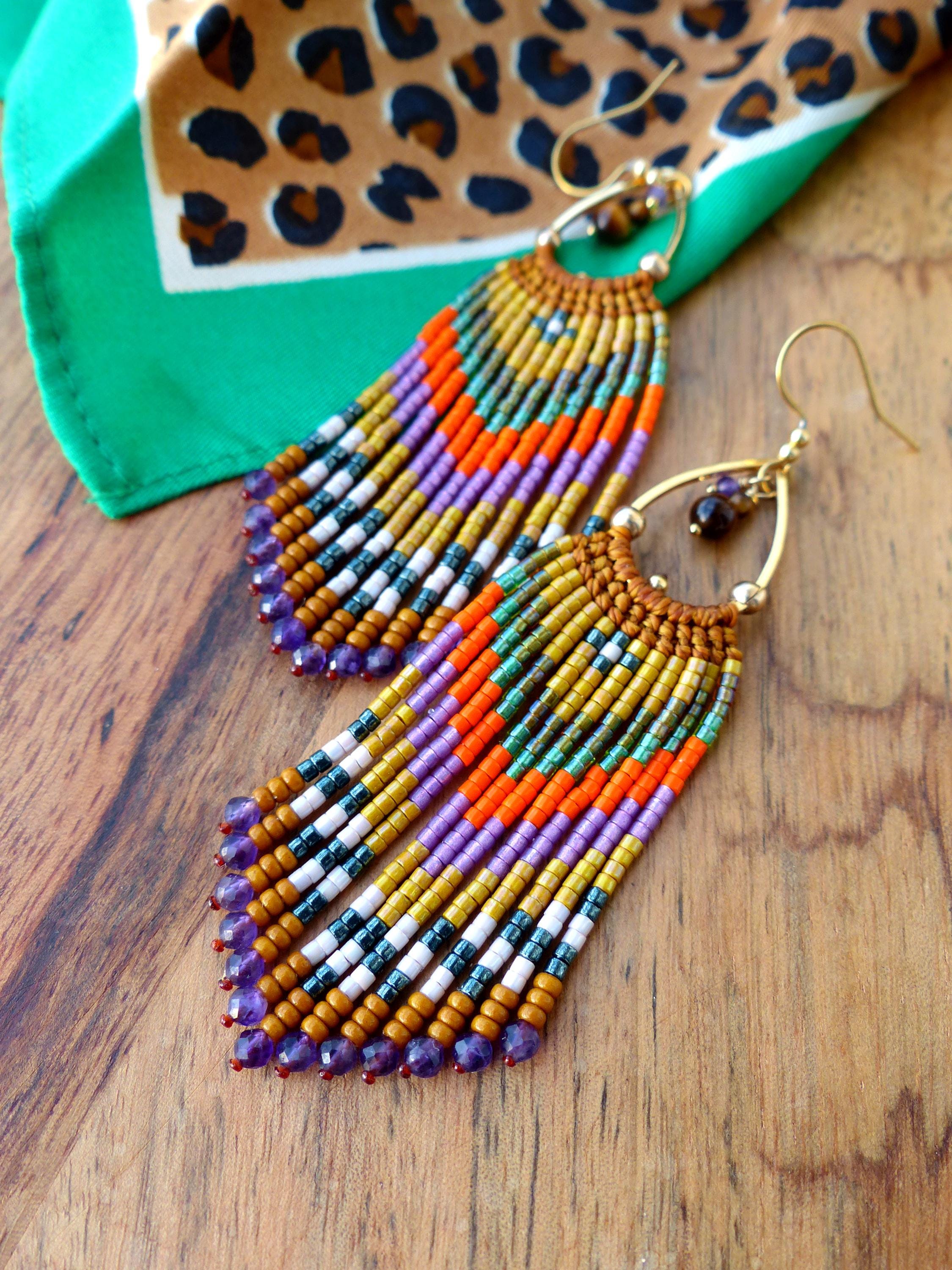 Peut inclure: Une paire de longues boucles d'oreilles en perles colorées avec une frange de perles d'améthyste. Les boucles d'oreilles sont faites avec une variété de couleurs, y compris l'or, l'orange, le violet, le vert et le blanc.