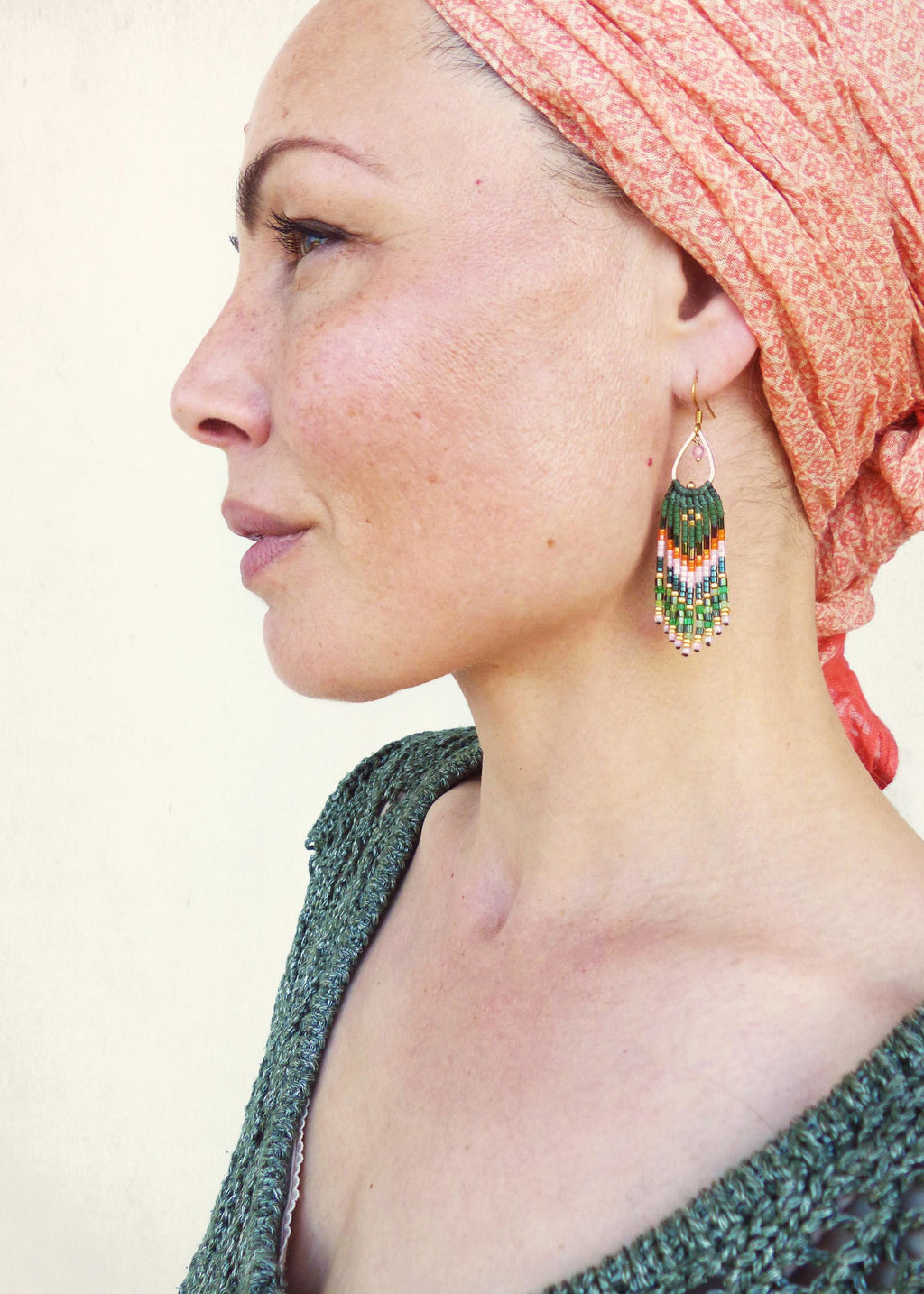 Peut inclure: Une femme portant un foulard de couleur pêche avec une boucle d'oreille à franges en perles vertes, blanches et orange.