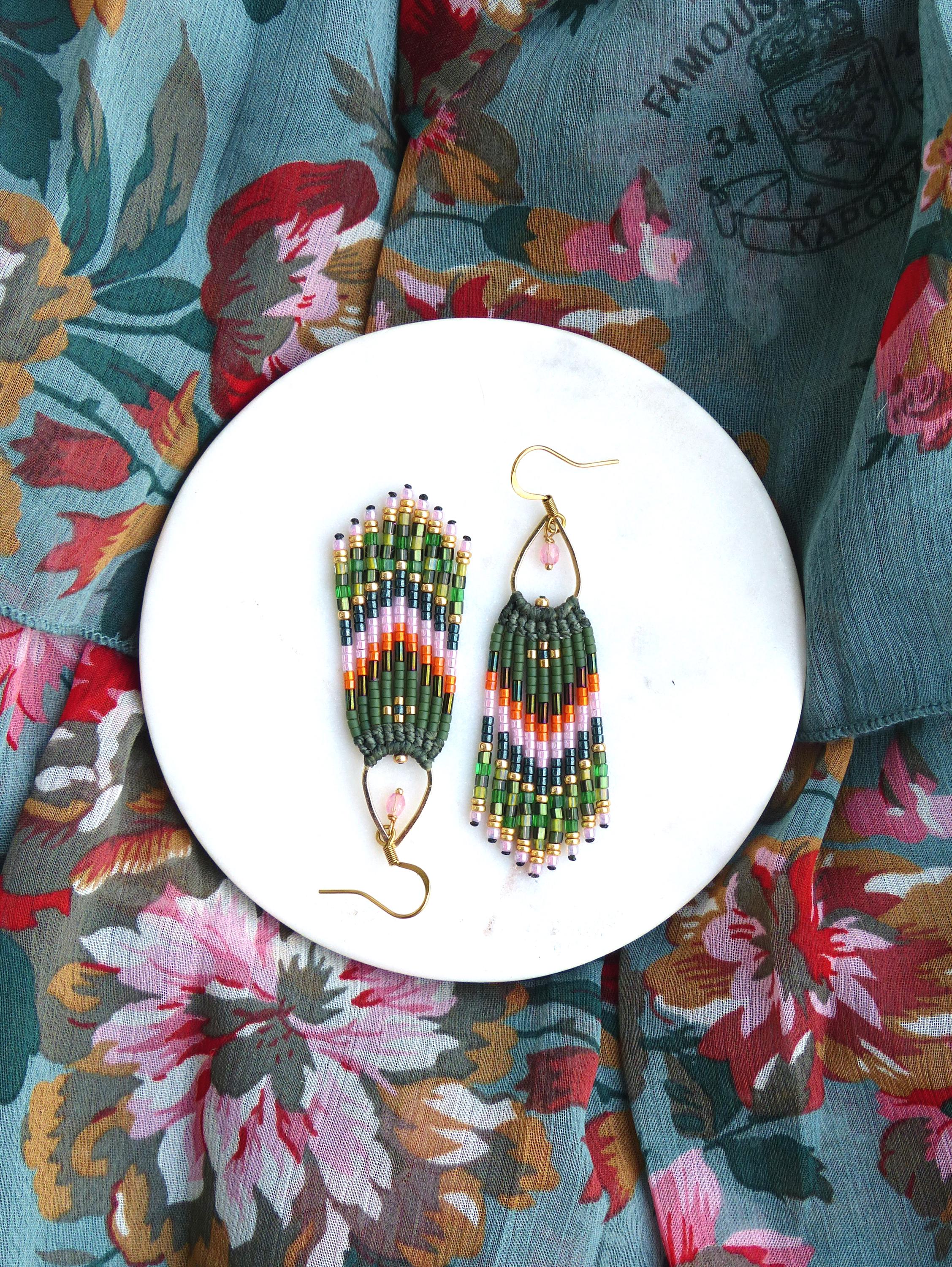 Peut inclure: Une paire de boucles d'oreilles pendantes en perles vertes, roses et dorées avec un accent de pierre rose. Les boucles d'oreilles sont sur une assiette blanche.