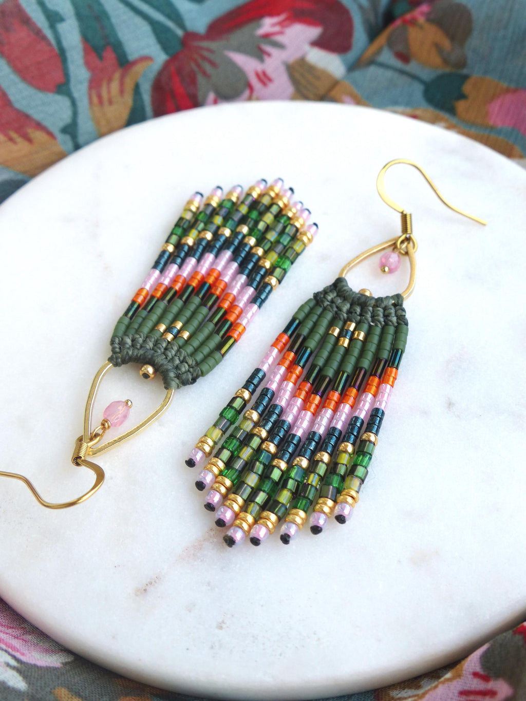 Peut inclure: Une paire de longues boucles d'oreilles en perles avec un crochet doré et une perle rose au sommet. Les perles sont vertes, roses, orange et noires.