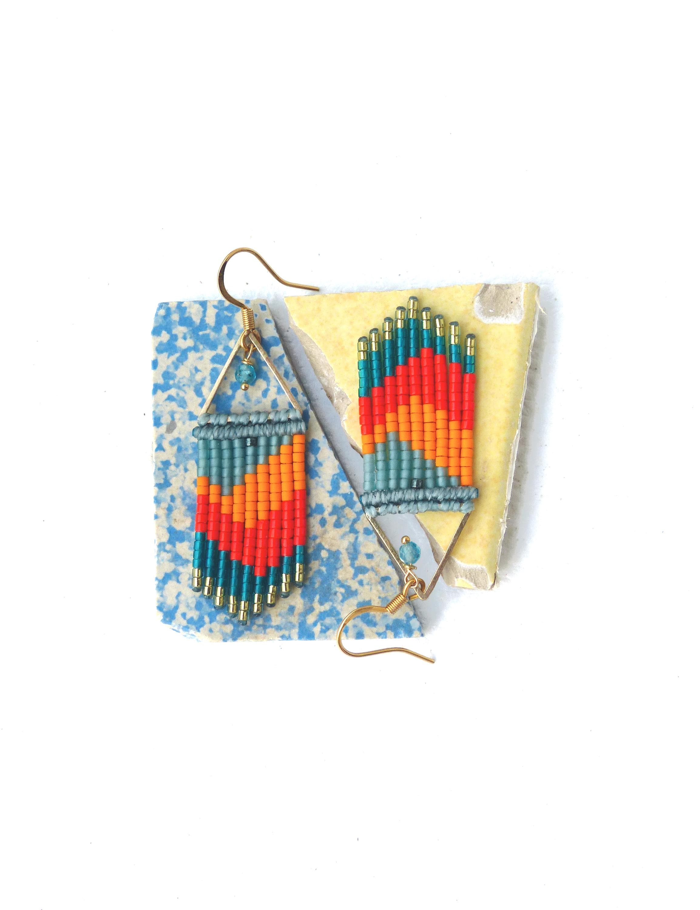 Peut inclure: Une paire de longues boucles d'oreilles en perles avec un motif géométrique dans des tons de bleu, orange et rouge. Les boucles d'oreilles sont suspendues à des crochets dorés.