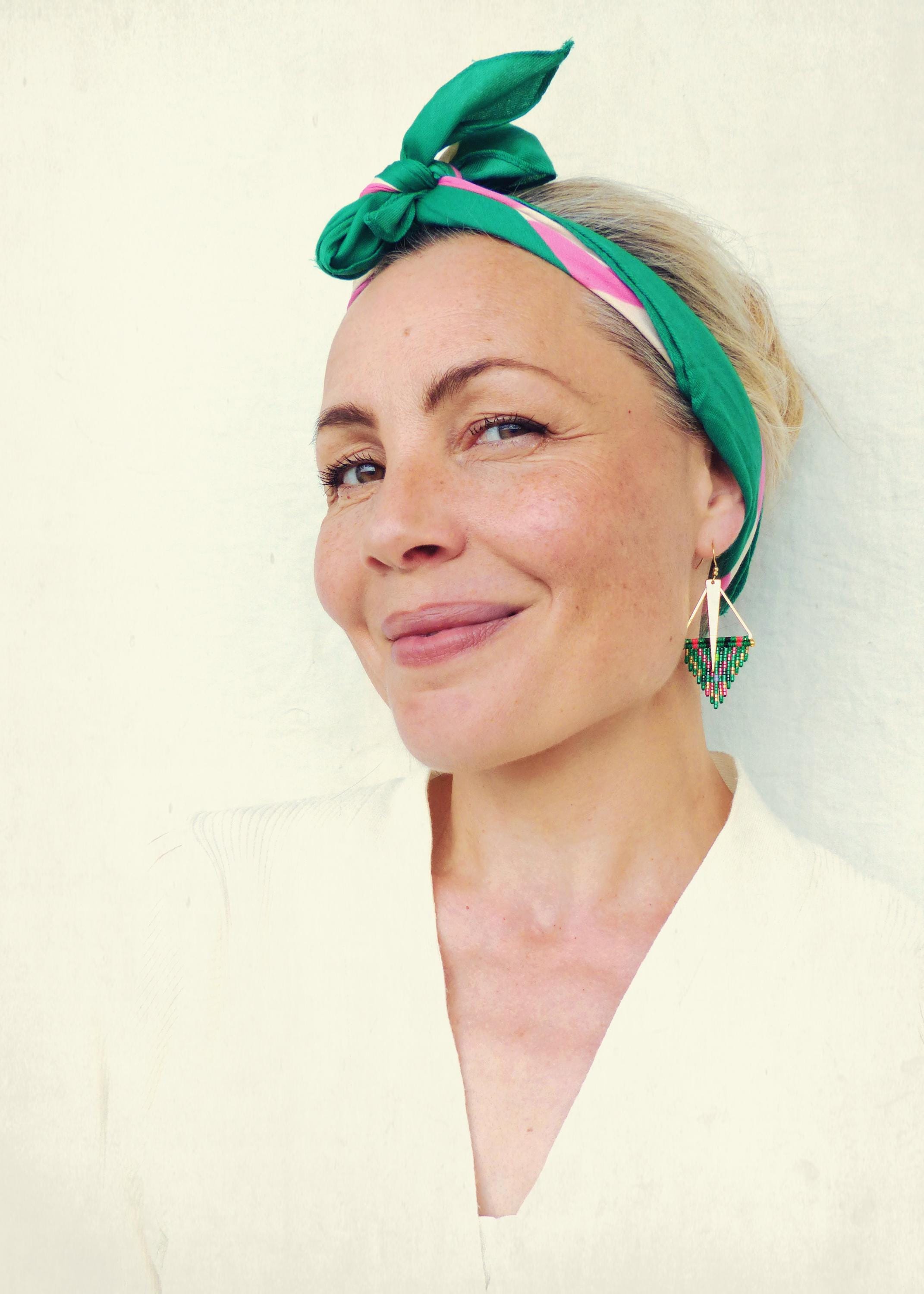 Peut inclure: Une femme portant un foulard à motifs verts et roses porte des boucles d'oreilles en perles vertes et roses. Les boucles d'oreilles sont en forme de triangle avec un long pendentif blanc fin suspendu au sommet.