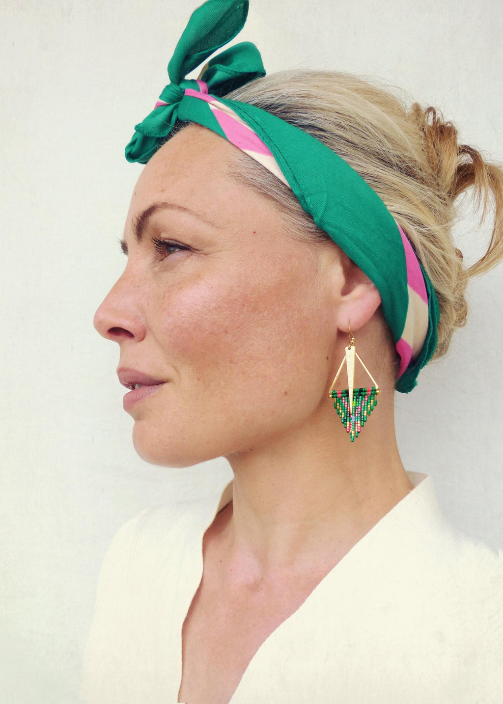 Peut inclure: Une femme portant un foulard à motifs verts et roses et une chemise blanche. Elle porte une paire de boucles d'oreilles géométriques en perles vertes et dorées.