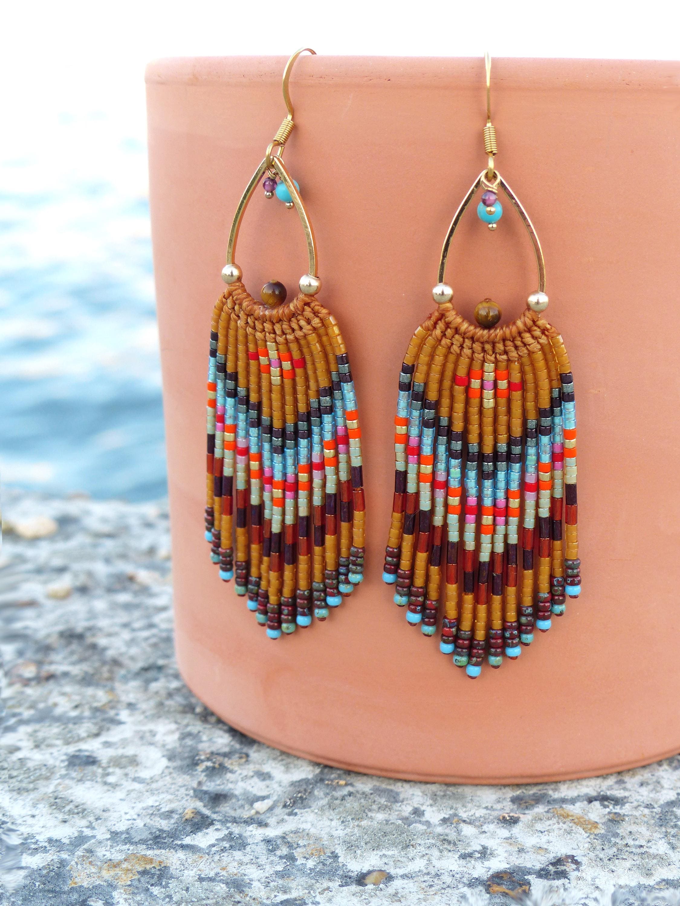 Peut inclure: Une paire de boucles d'oreilles faites à la main avec une monture en métal doré. Les boucles d'oreilles présentent un design à franges avec un mélange de perles colorées dans les tons de marron, orange, bleu et rouge. De petites perles turquoise et violettes ornent le haut.